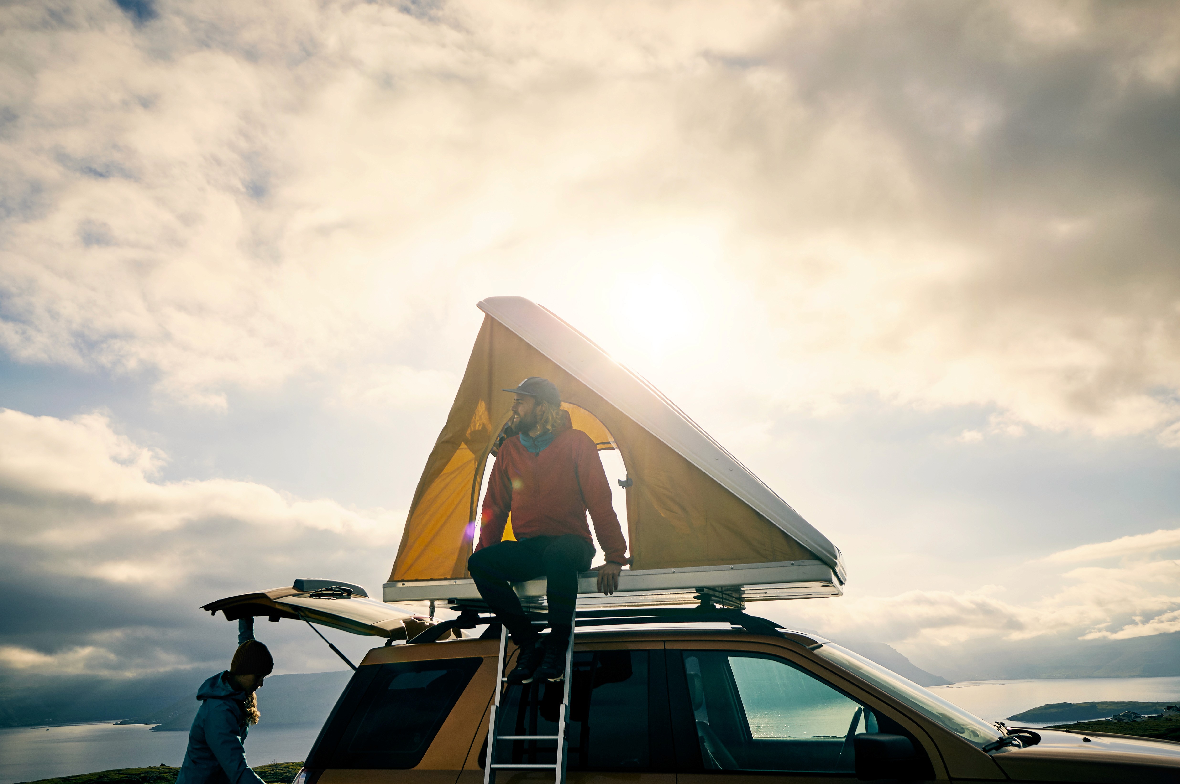 "Person setting up rooftop tent on camper van under cloudy sky - active outdoor lifestyle"