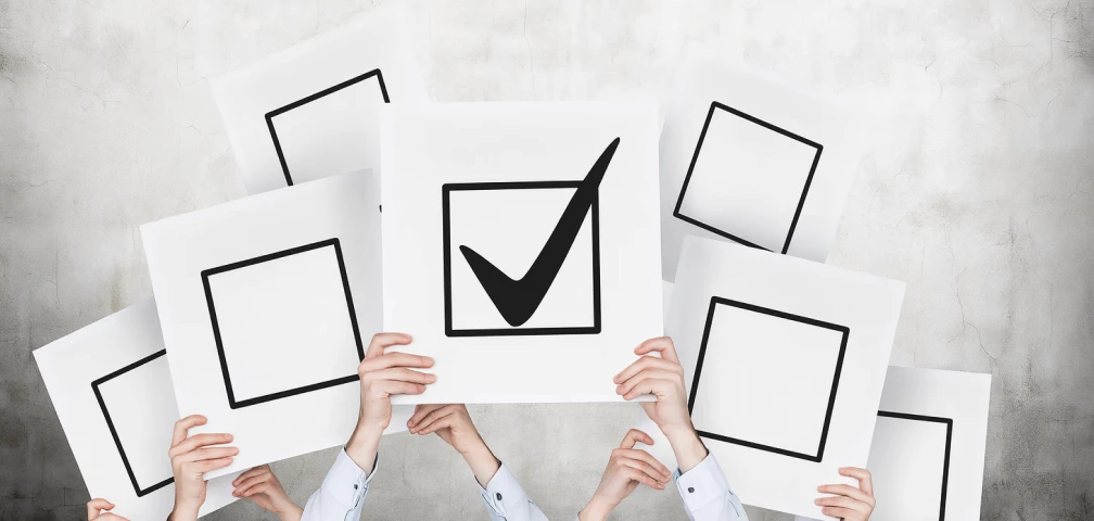Multiple hands holding up square signs, one with a bold checkmark symbol, representing approval, completion, or standing out from the crowd