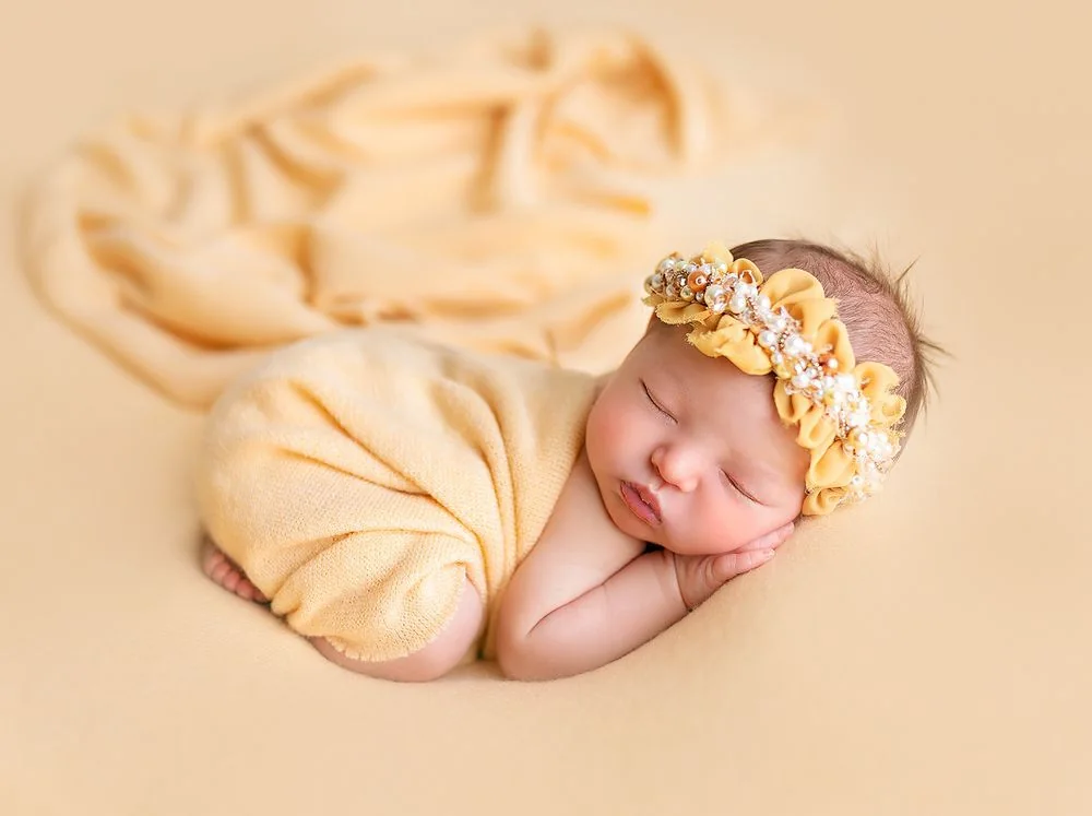 Sleeping newborn in a yellow wrap and floral headband