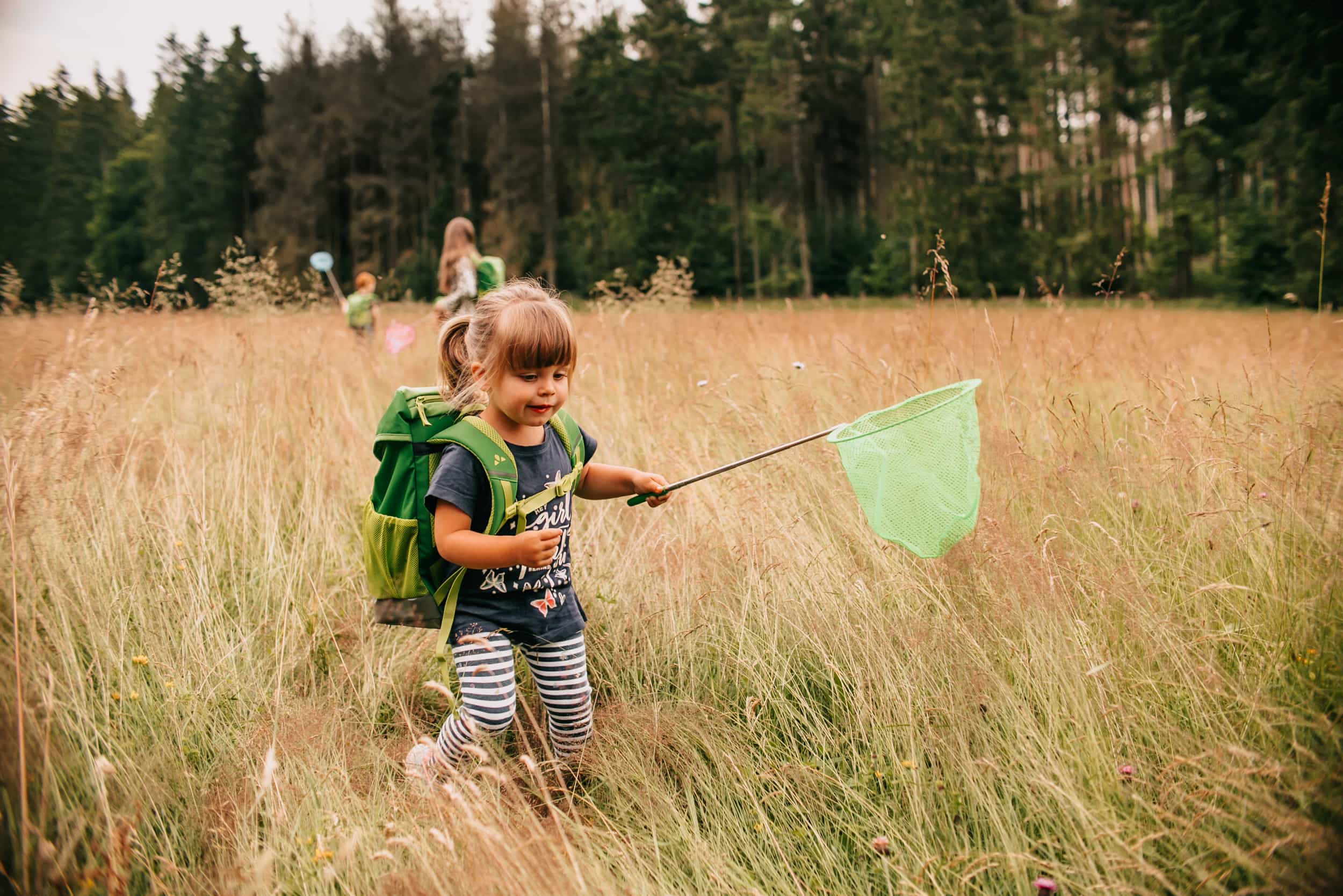Girl with a fan runs with the green backpack across a field
