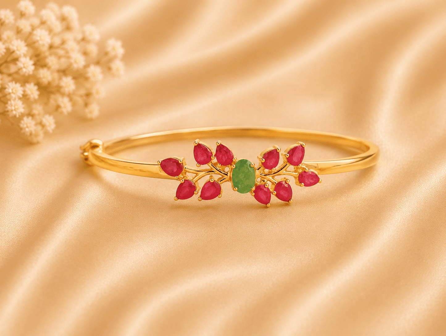 A gold bracelet with ruby and emerald accents rests on a silky, cream-colored fabric.