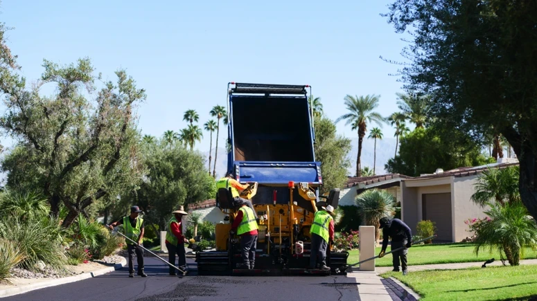 Asphalt paving crew refilling paving machine with material while rakers edge up new overlay