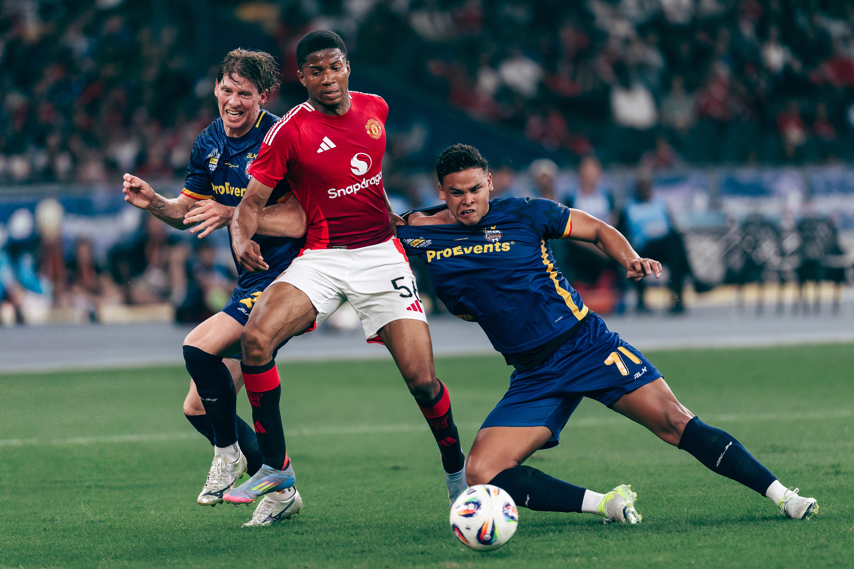 Harrison Delbridge, Chido Obi, and Irfan Fandi, engage in a tussle in a match between Manchester United and the ASEAN All Stars at the Maybank Challenge Cup 2025