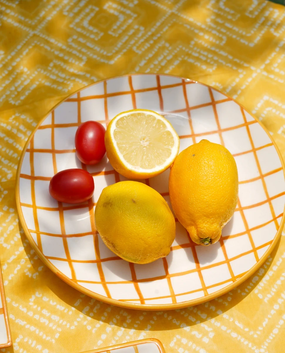 Styled plate of lemons and tomatoes on a yellow patterned tablecloth.