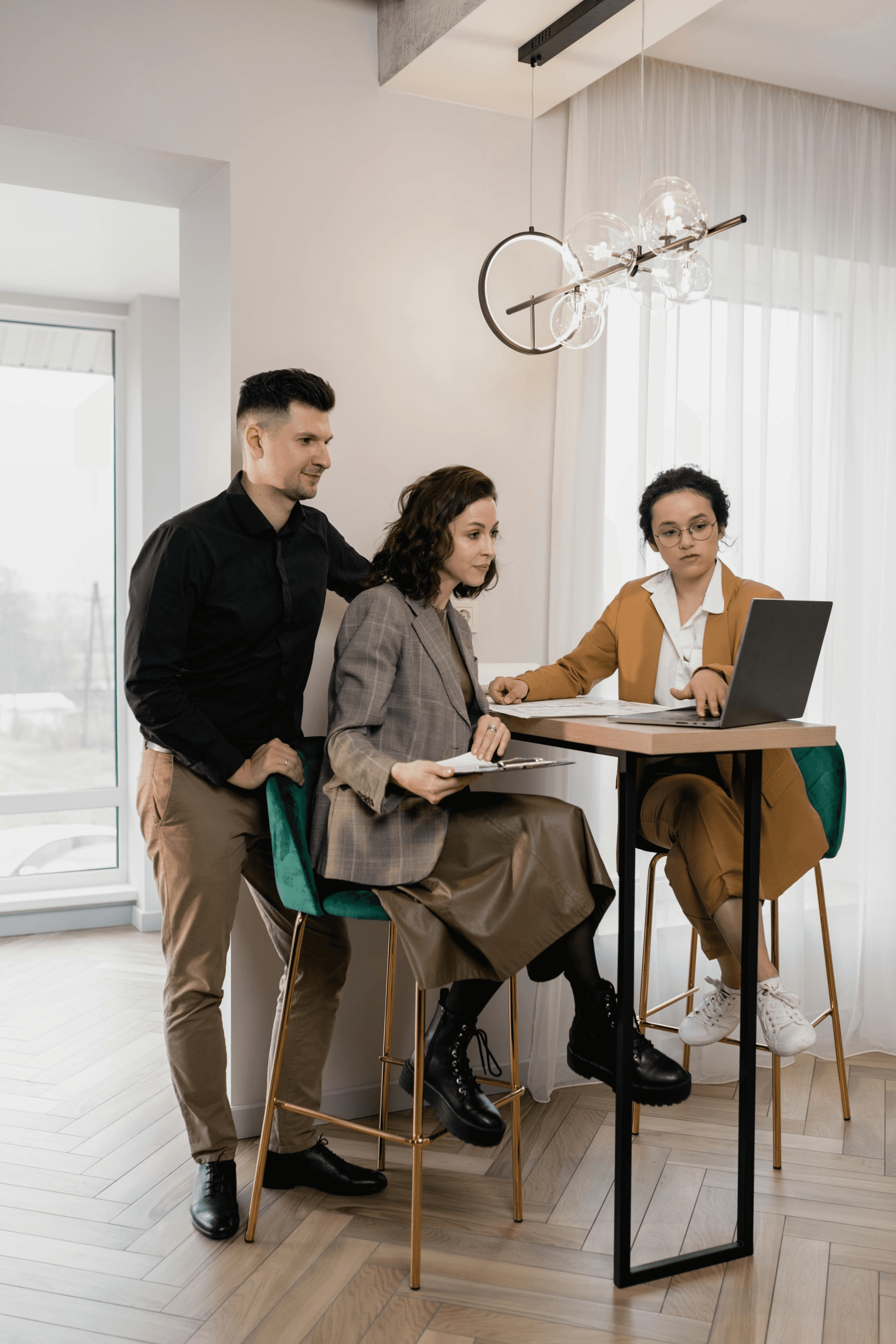 Three people collaborate around a laptop at a modern workspace, discussing ideas and solutions.