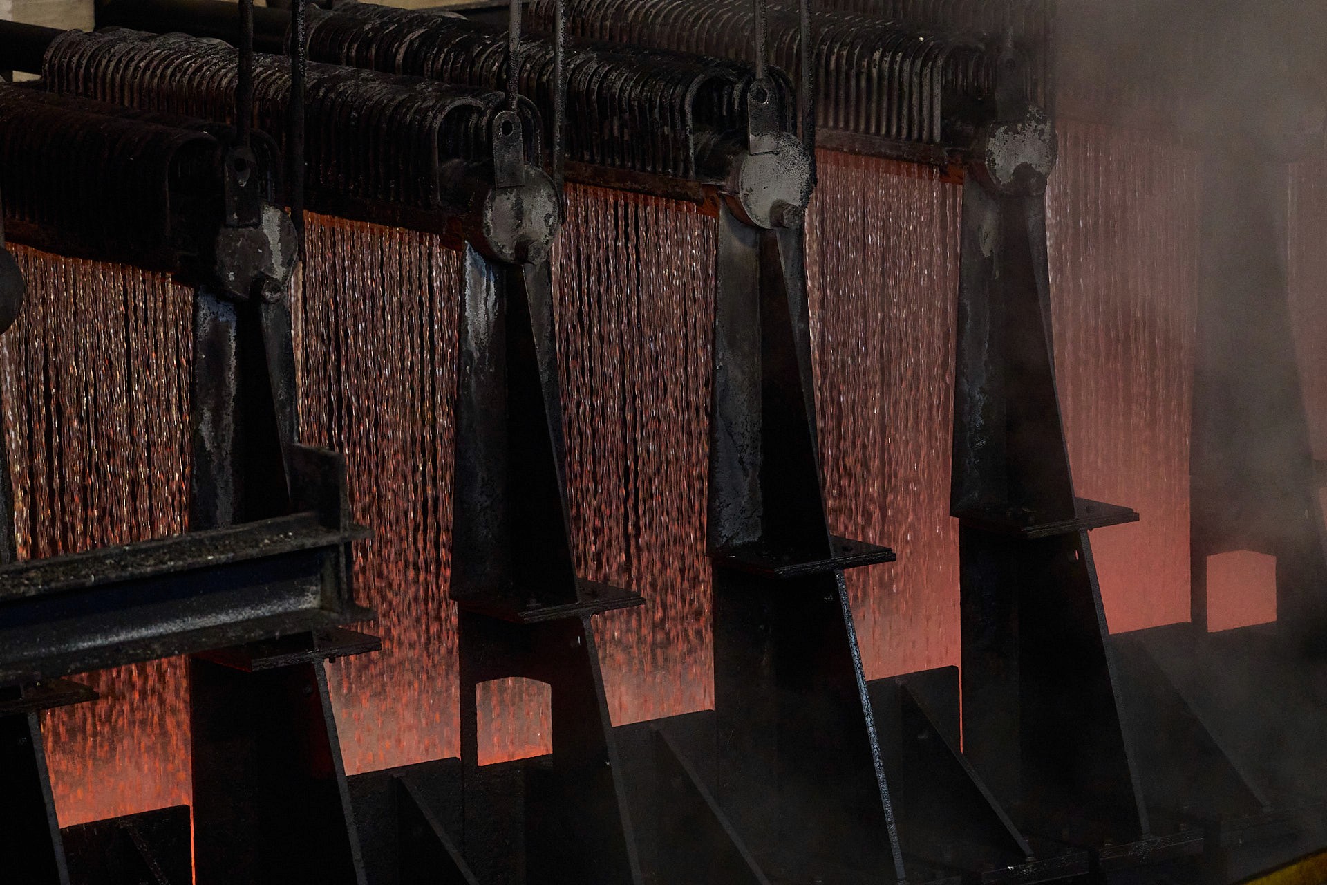 Vue sur un laminoir industriel avec une plaque d'acier en fusion rouge vif le traversant de gauche vers la droite, générant de la fumée et des projections d'eau.