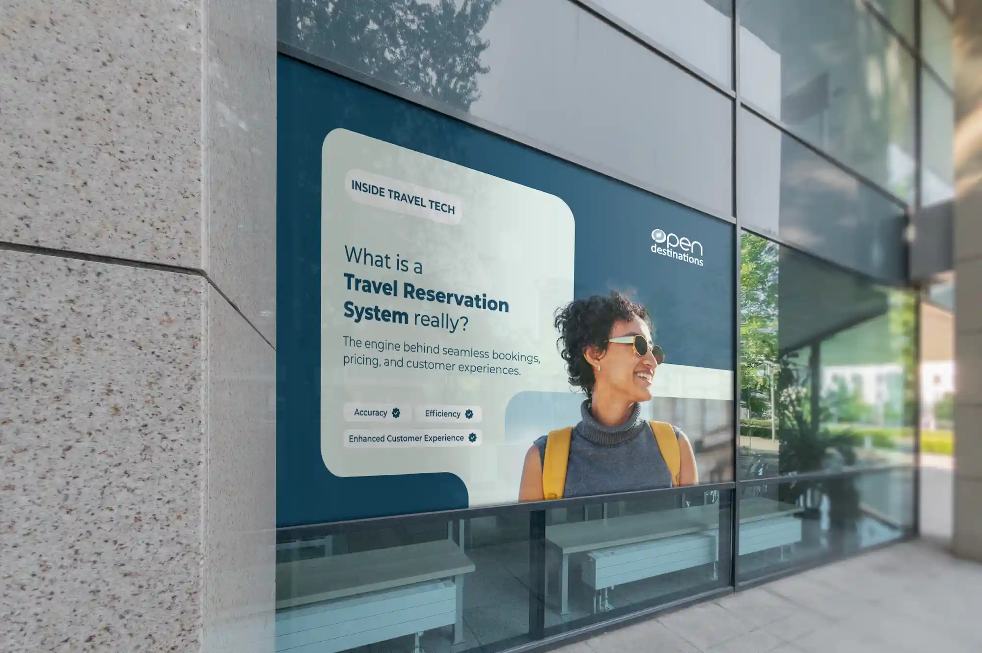 Large outdoor window graphic for Open Destinations showing a smiling traveller wearing sunglasses. The display reads: “What is a Travel Reservation System really? The engine behind seamless bookings, pricing, and customer experiences.”