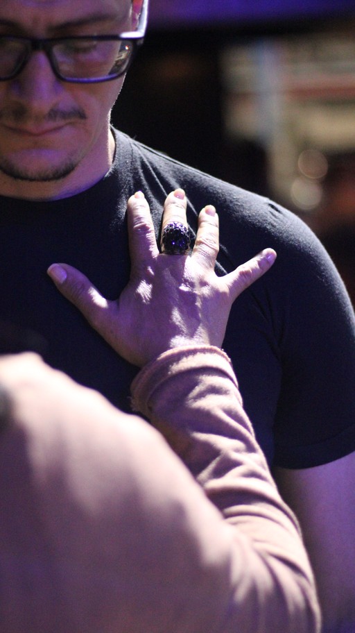 A group of people sitting on grass under trees, enjoying a sunny day near a body of water.