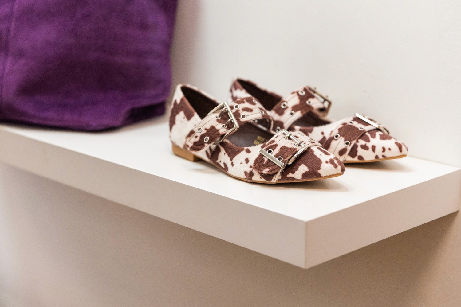 Brown and white print flat shoes on a bright studio shelf.