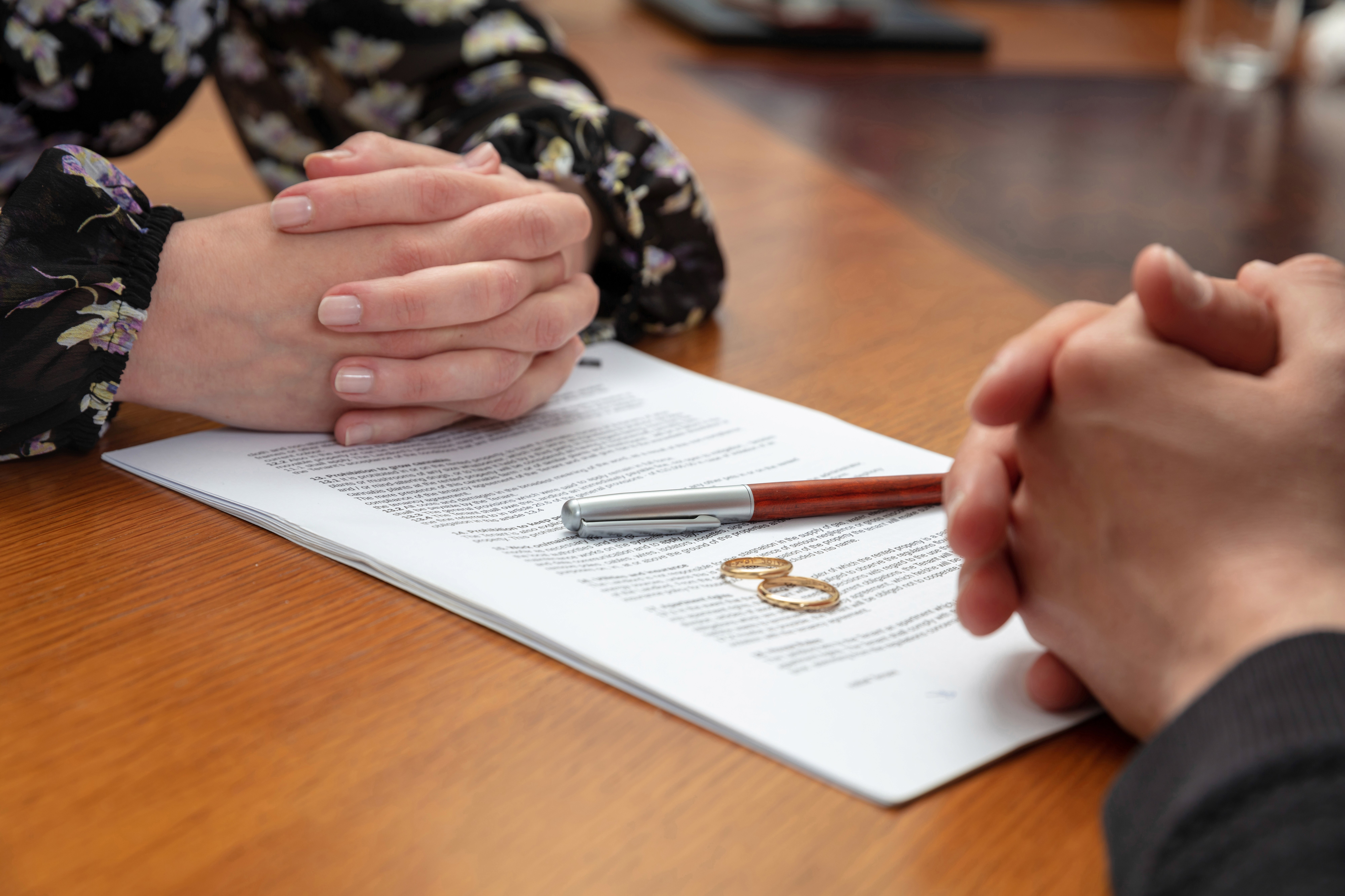 Two people with clasped hands across a table with divorce documents and wedding rings, representing high net worth divorce proceedings in Salem, MA