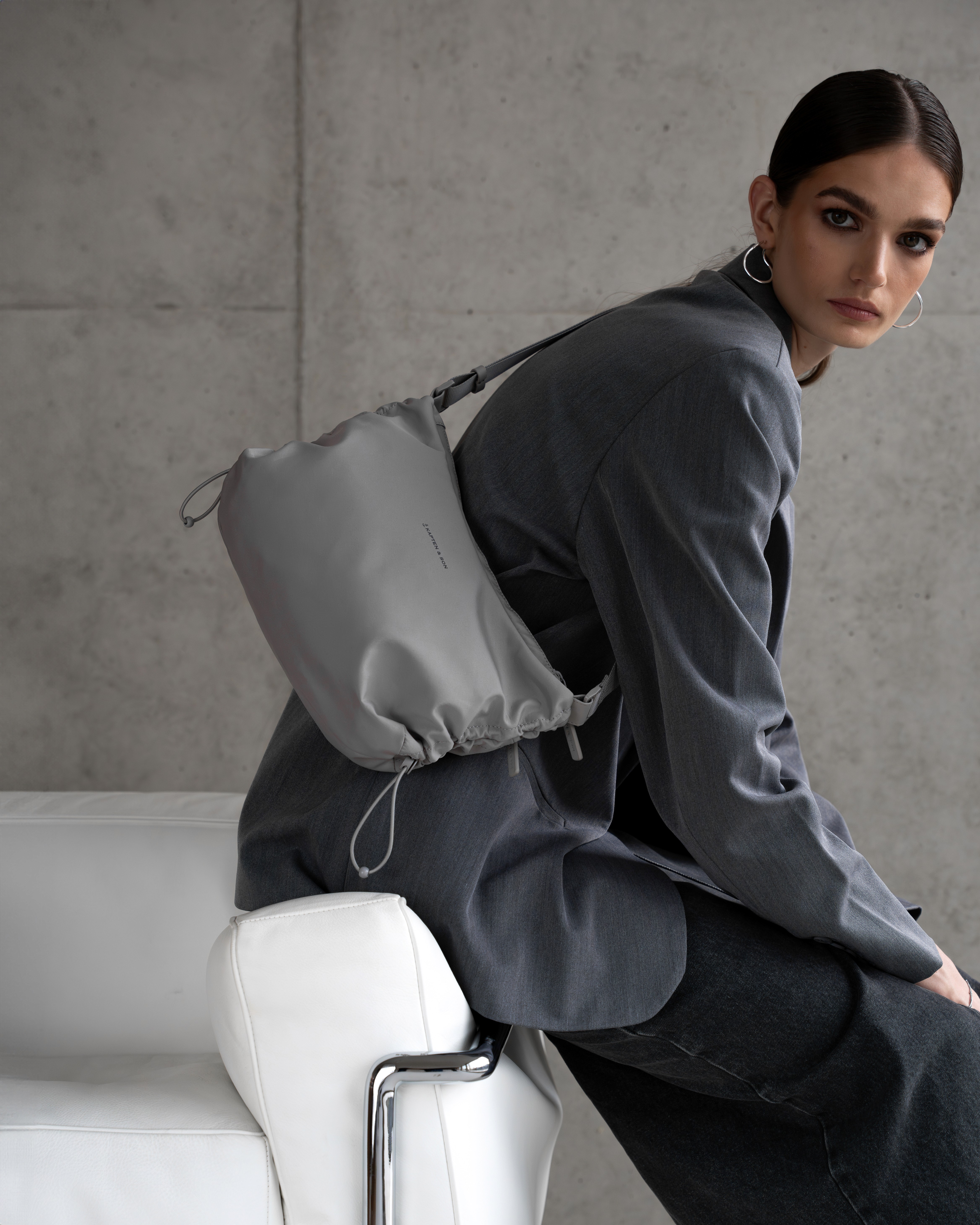 Une femme porte un sac à main sportif gris clair, assise sur un canapé blanc