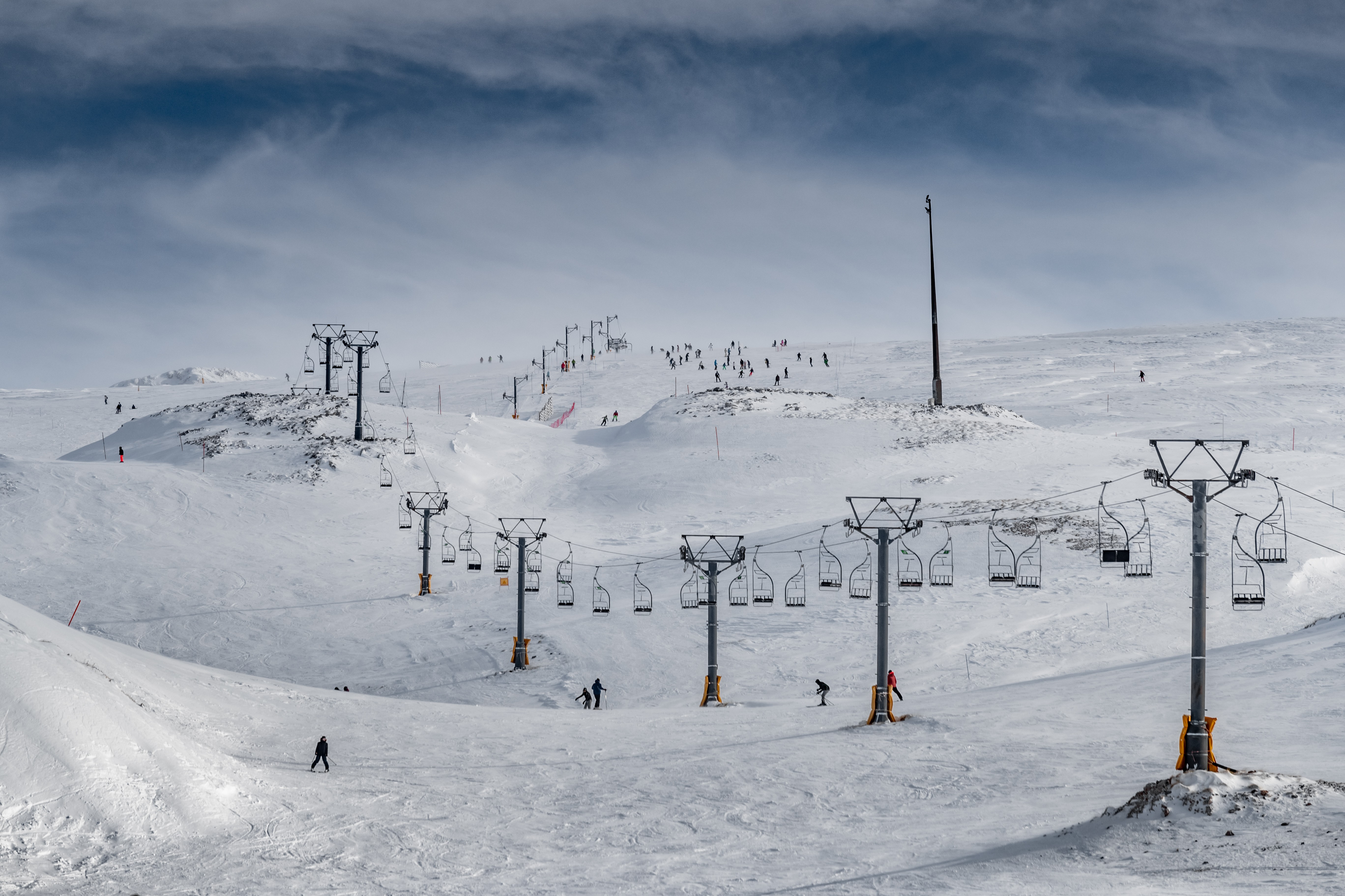 Skiers spread across wide open slopes beneath multiple chairlifts on a bright winter day.