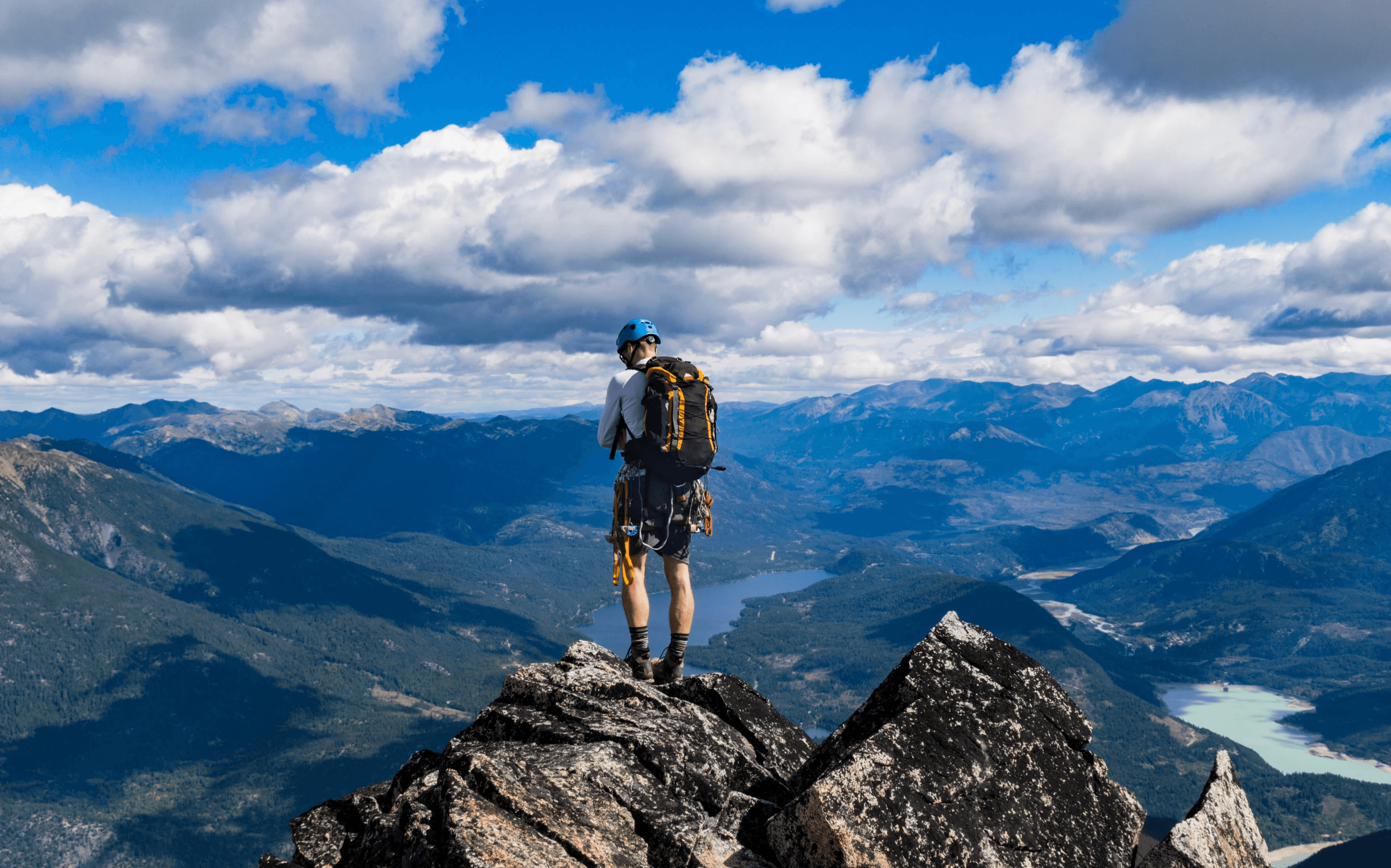 Hiker standing on a rocky mountain peak overlooking a valley and lakes.      Like  Dislike