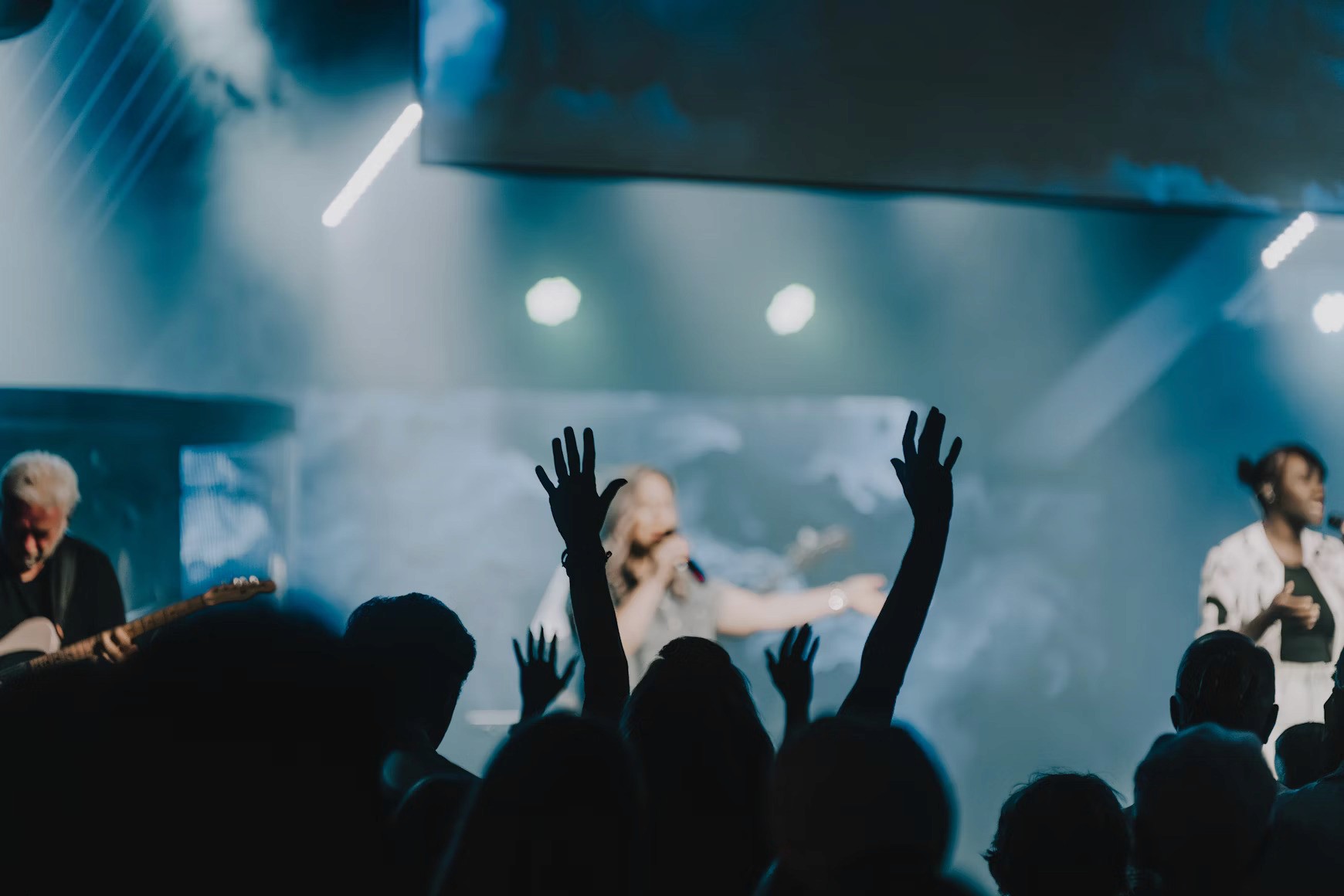 Concert audience with raised hands enjoying live music performance on stage.