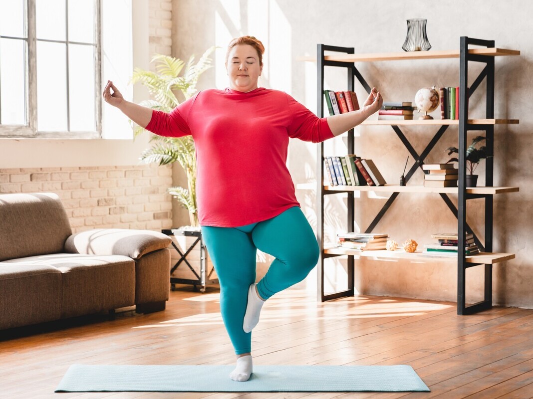 woman focusing on holding a pose while losing weight with yoga on a mat in a sunny room at home