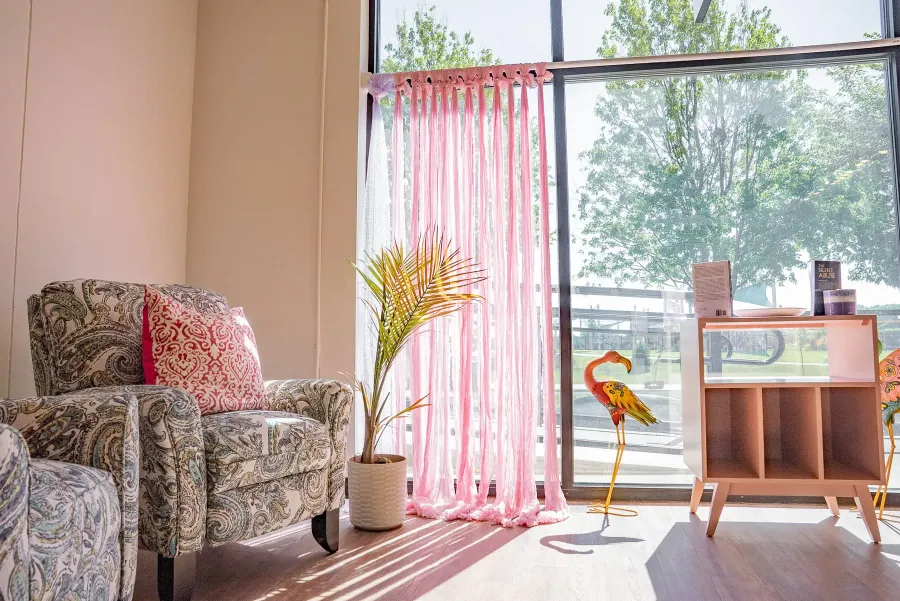 A cozy studio corner with a patterned armchair and soft pink curtains.