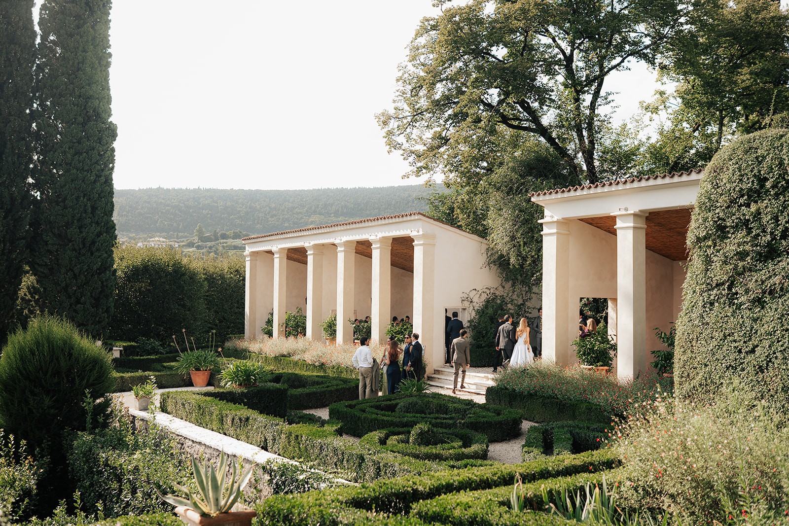A scenic view of a garden with neatly trimmed hedges and trees, featuring a modern building in the background.