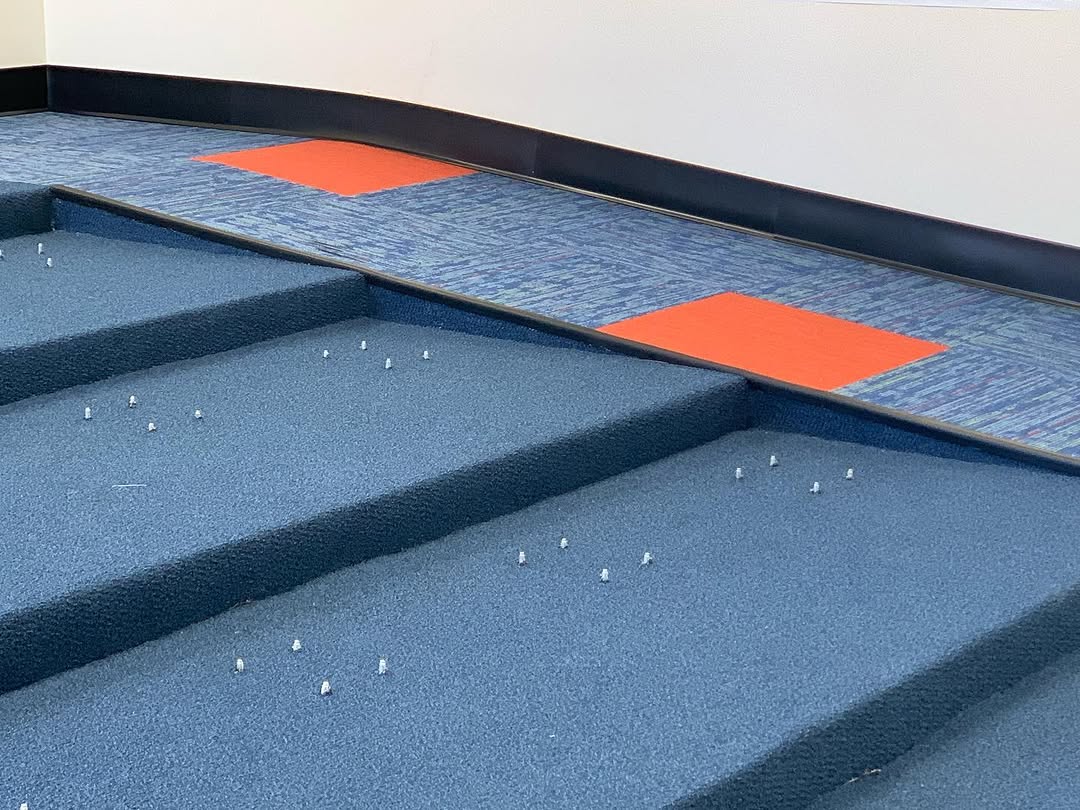 Blue carpet tile laid across conference room tiers with orange accent inserts