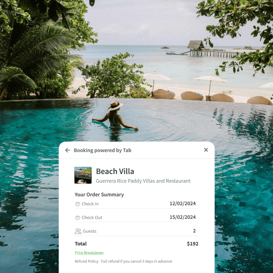 Woman wearing a hat relaxing in an infinity pool overlooking a tropical beach with white sand, umbrellas, and turquoise water.