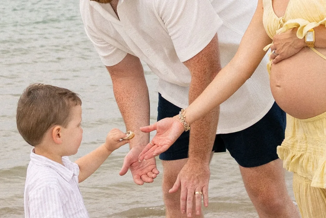 Little boy handing a seashell to his parents at the water's edge, by Sioux Falls, SD family photographer Kelsey Lynn