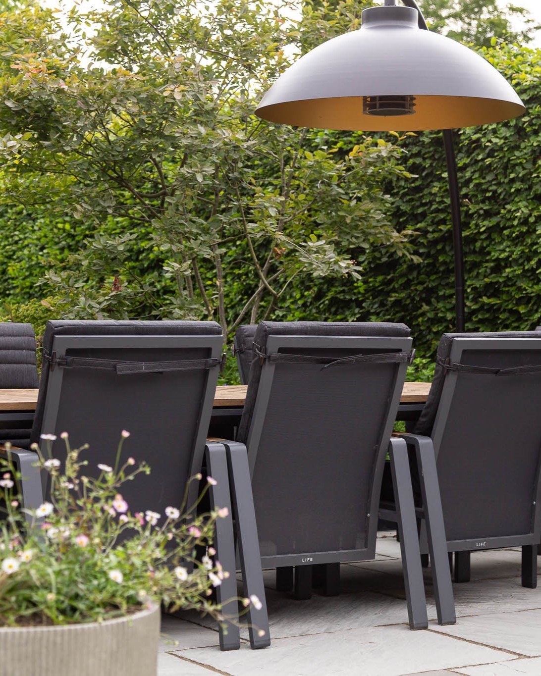 A stylish outdoor seating area with black metal and timber garden furniture, including a dining table and a modern freestanding dome patio heater from Heatsail.