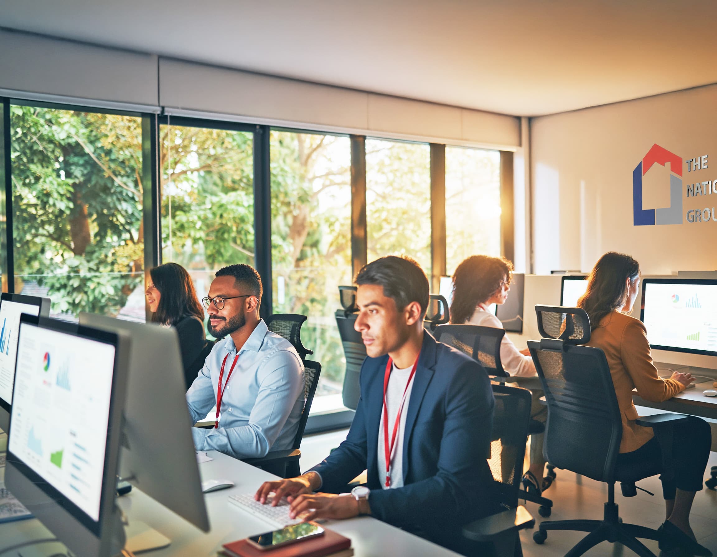 The team working at their desks on computers in front of the wall of windows. 