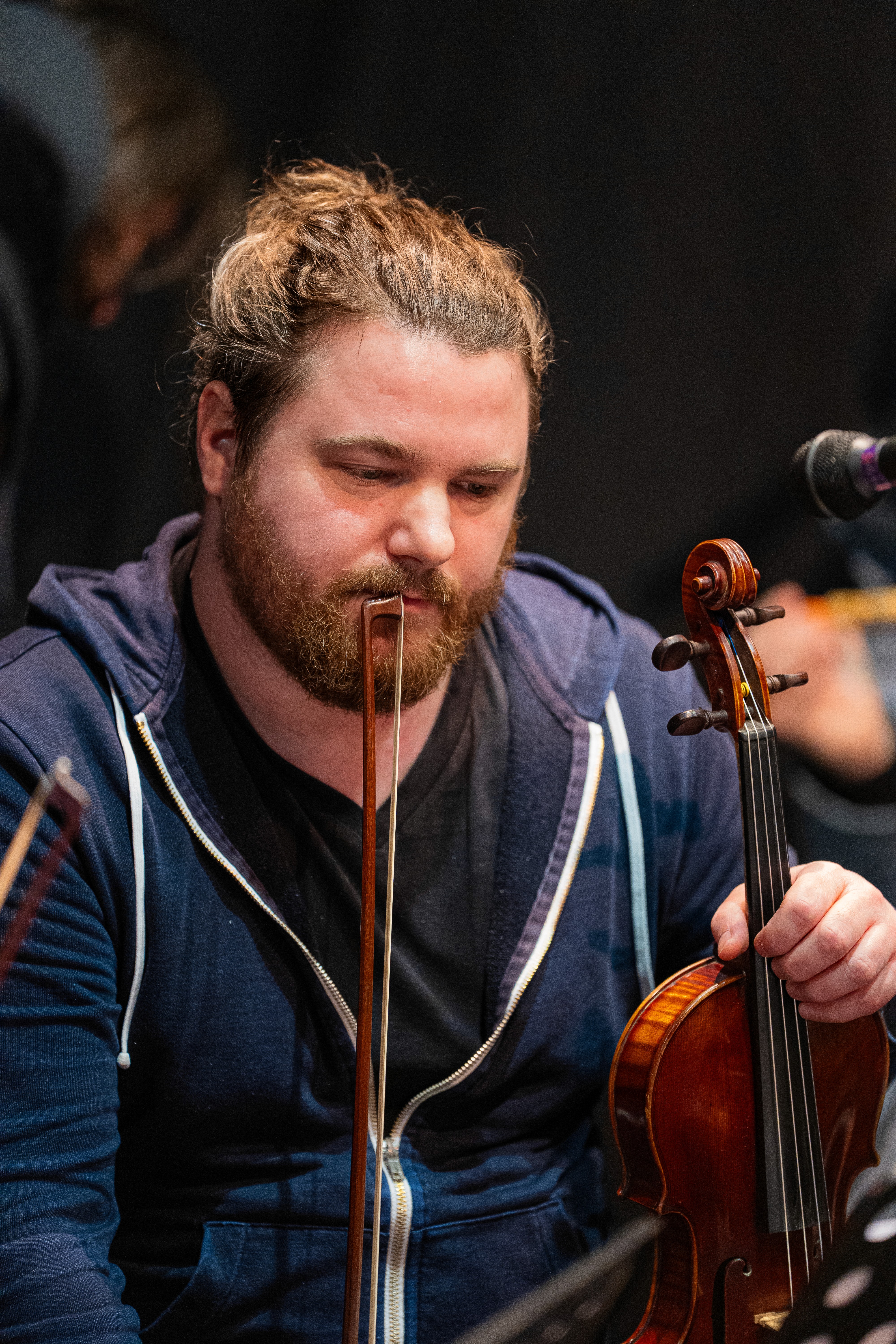 A woman in a white blouse and dark vest sits on a park bench, looking away and smiling. A ukulele rests next to her.