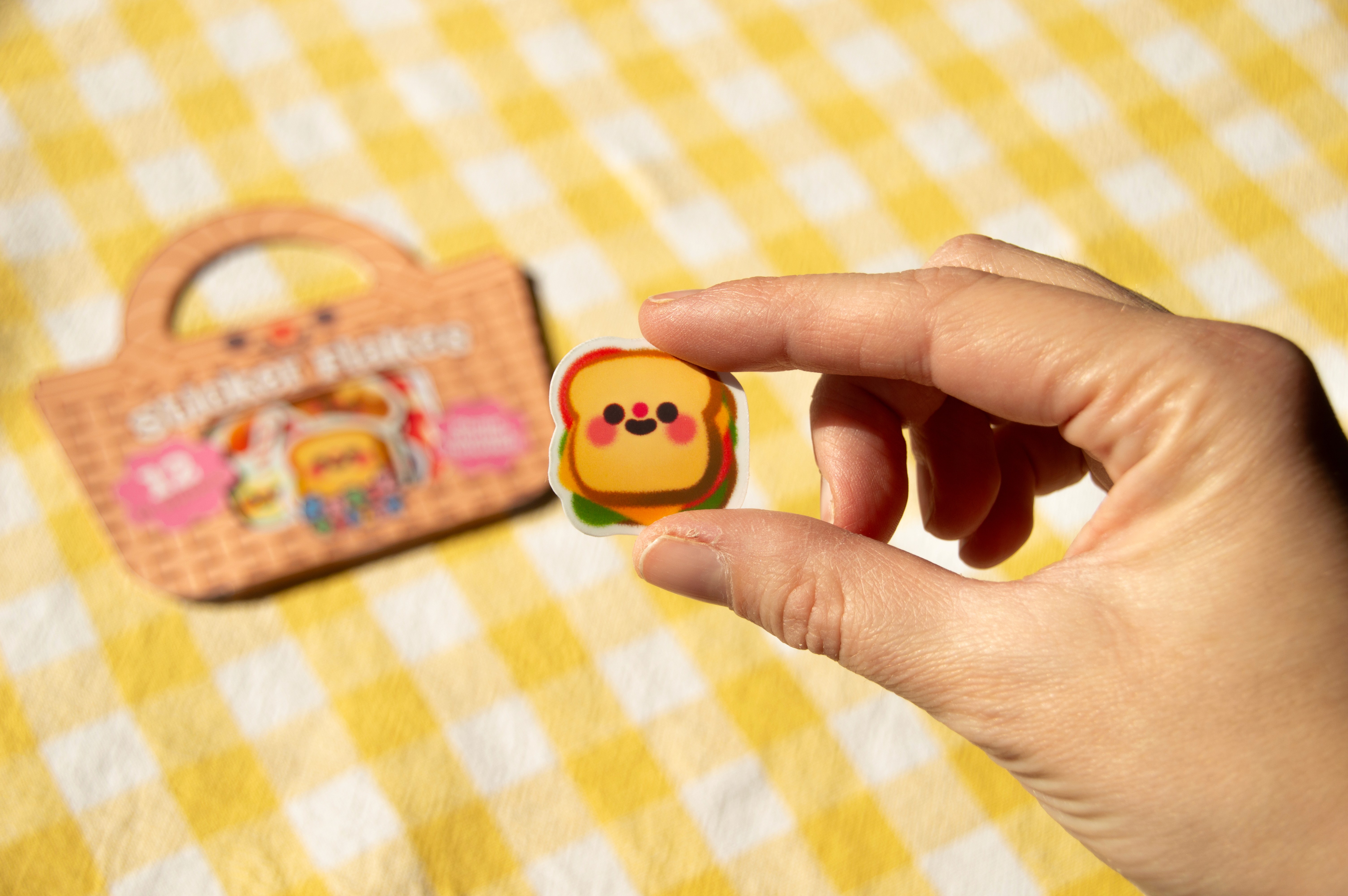 A hand holding a very small sandwich sticker.