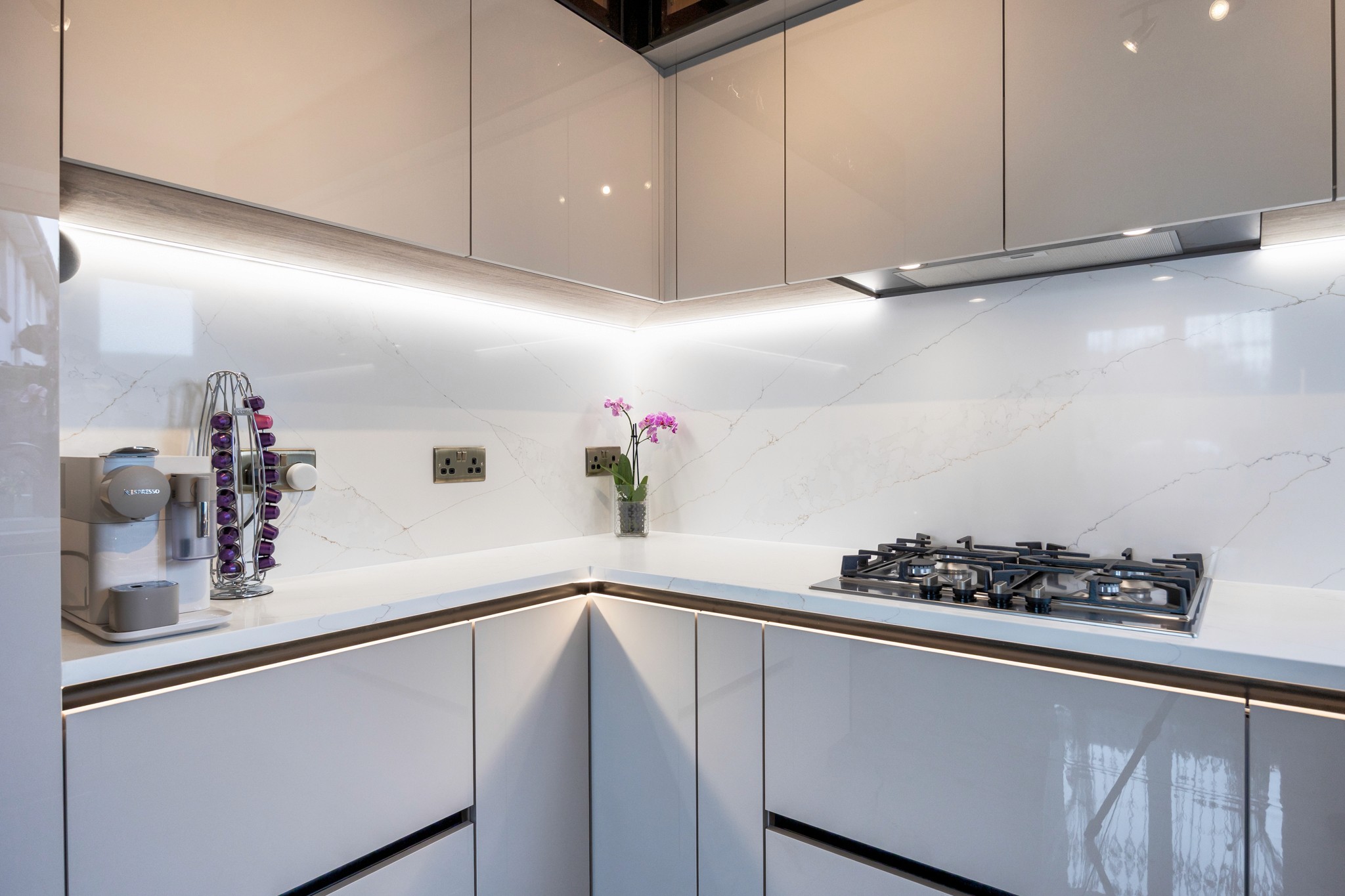 Modern two-story home with large glass windows, warmly lit interiors, and a balcony. Surrounded by trees and a manicured lawn at dusk. Cozy ambiance.