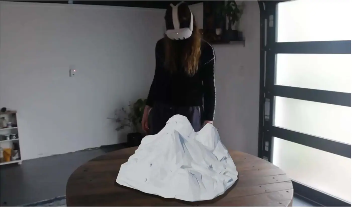 A person in a headset standing over a virtual mountain on a real table