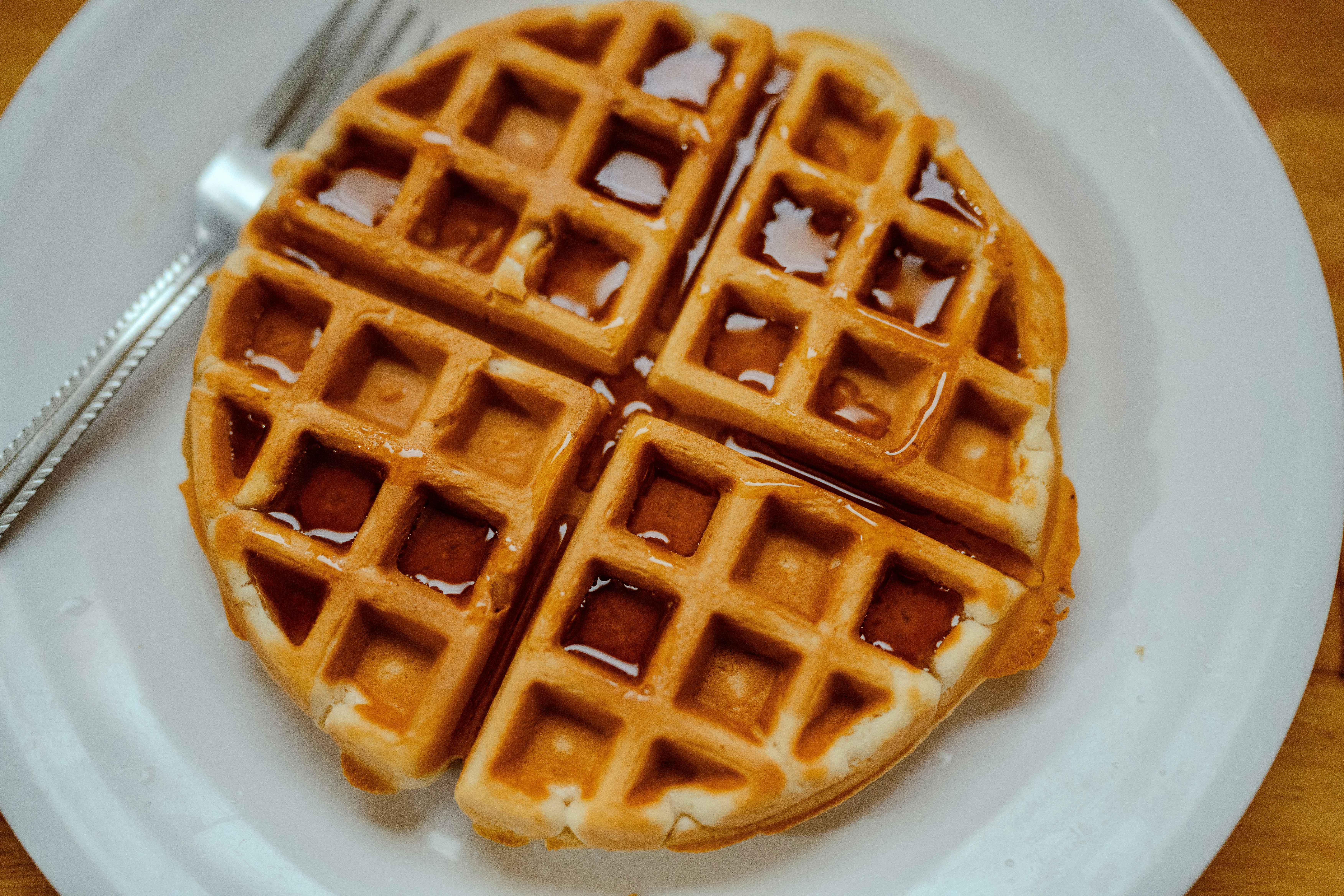 A golden waffle topped with syrup on a white plate