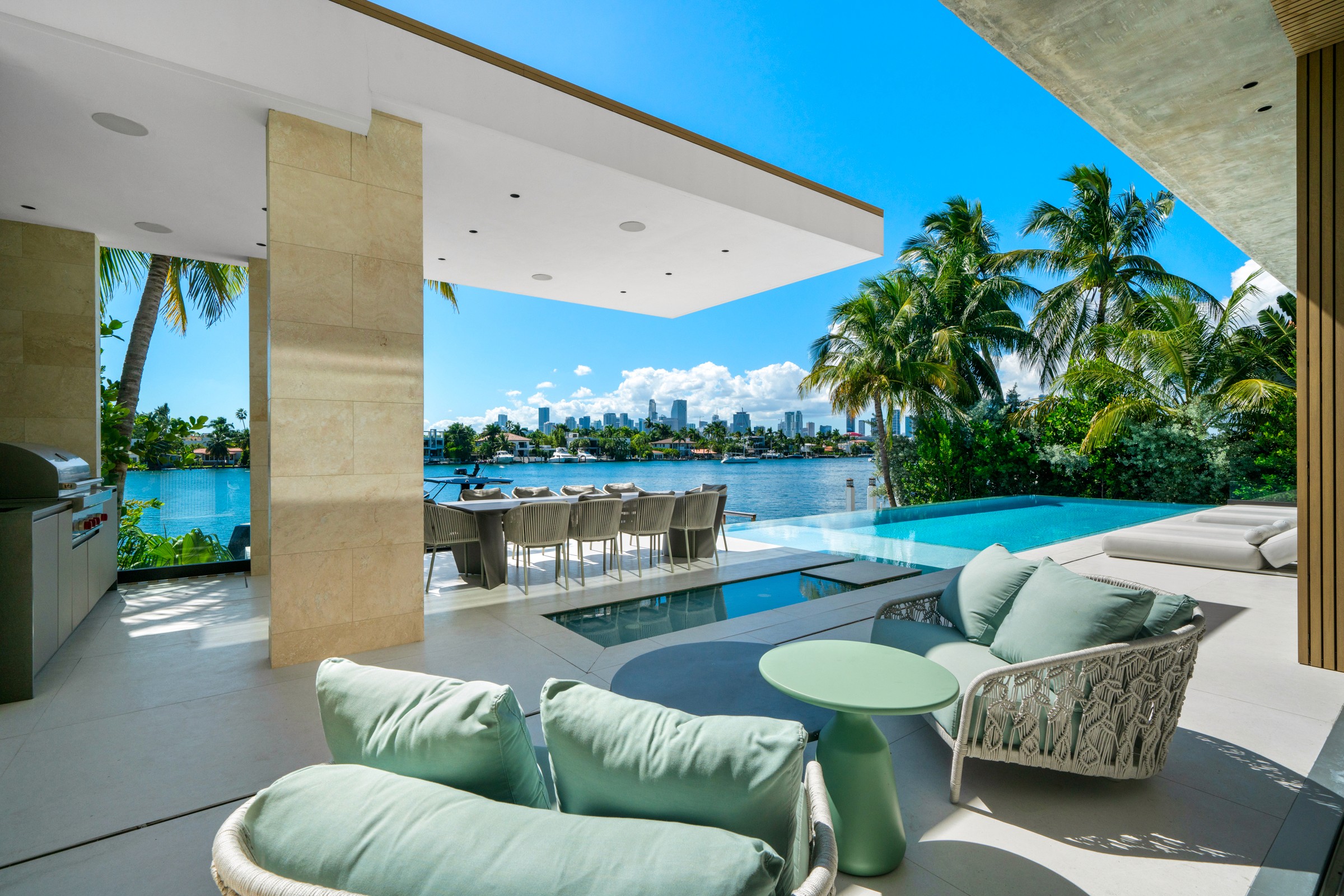 A luxurious patio with comfortable seating, lush greenery, and a pool overlooking a serene waterfront.