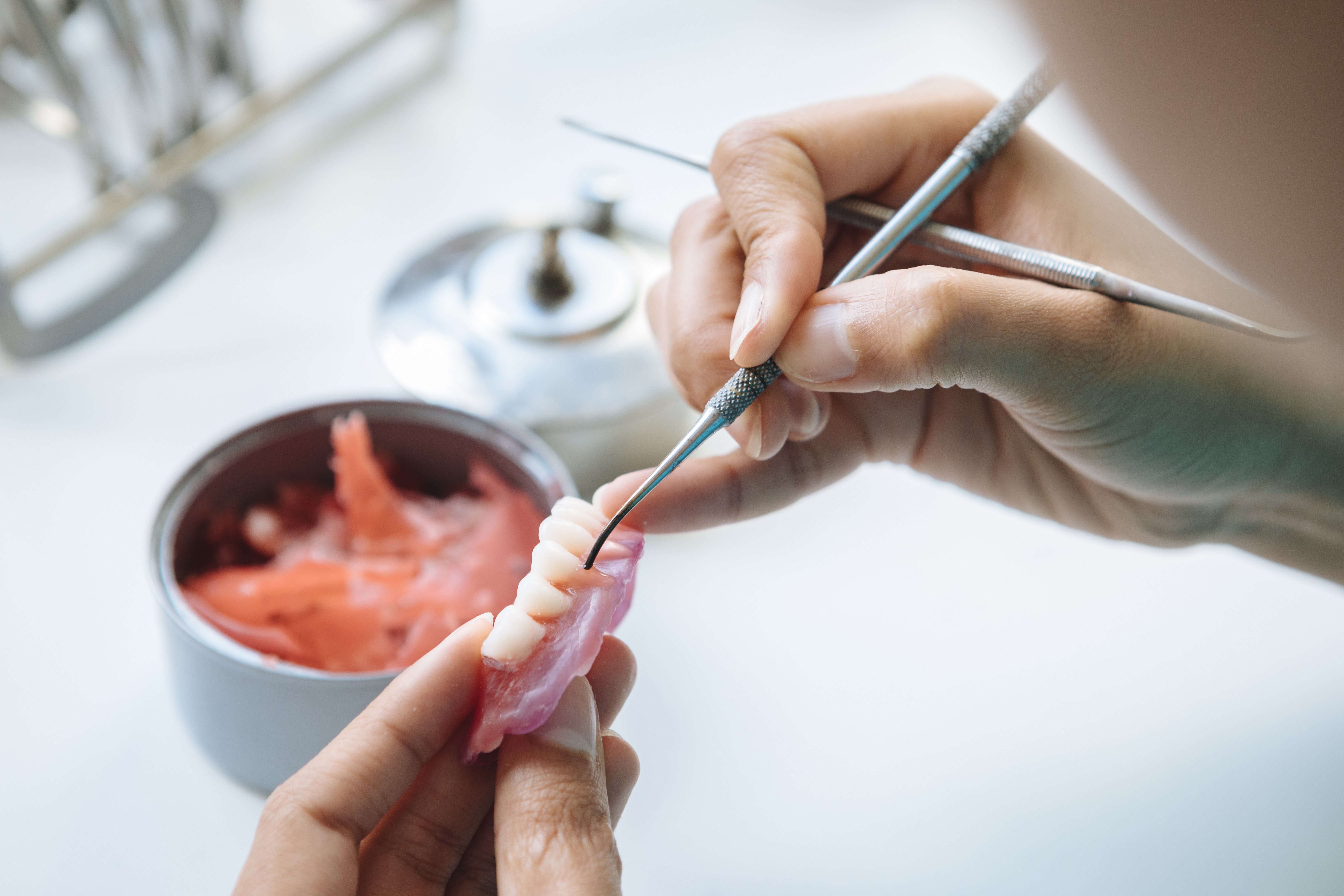 Detailaufnahme eines Zahntechnikers beim Modellieren einer Zahnprothese im Dentallabor.