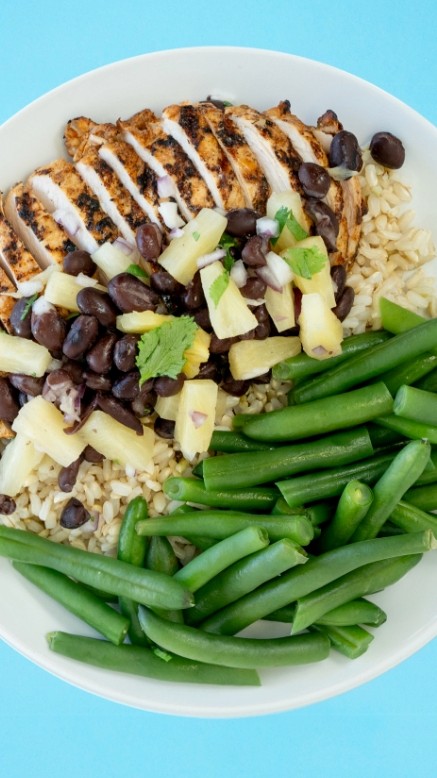 Plate of grilled chicken, on a bed of rice with steamed beans and a side of house-made pineapple black bean salsa on a blue background.