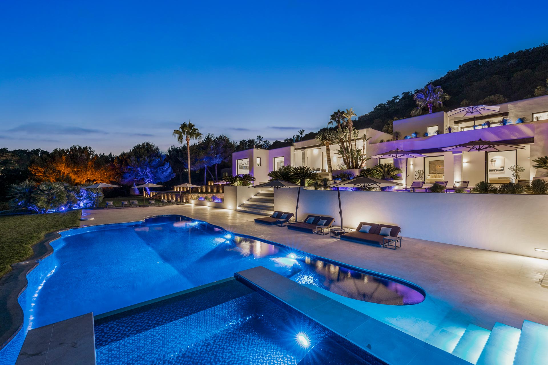 Luxury Ibiza villa at dusk with illuminated pool, terraces and landscaped gardens overlooking the Mediterranean.