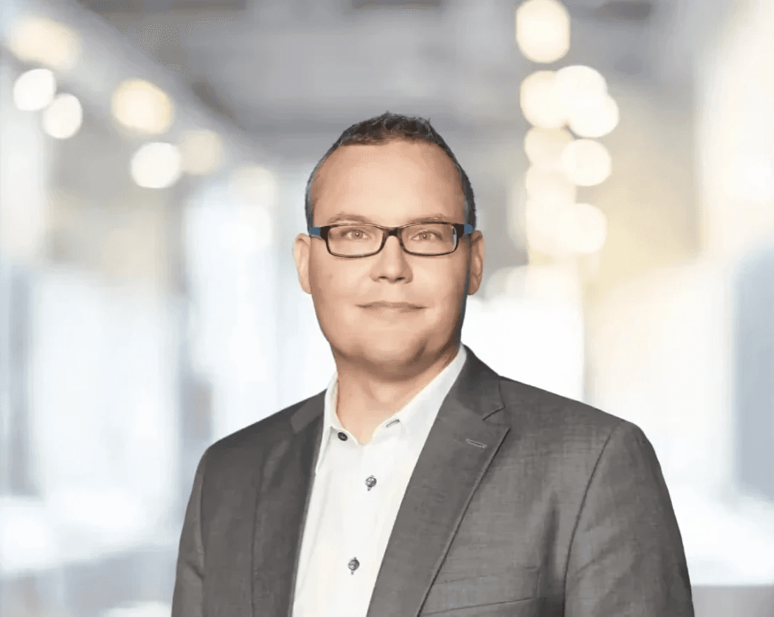 Dr. Johannes Rückert, Vorstand KWA Kuratorium Wohnen im Alter gAG, Portrait eines Mannes mit Brille im grauen Anzug vor unscharfem Bürohintergrund.