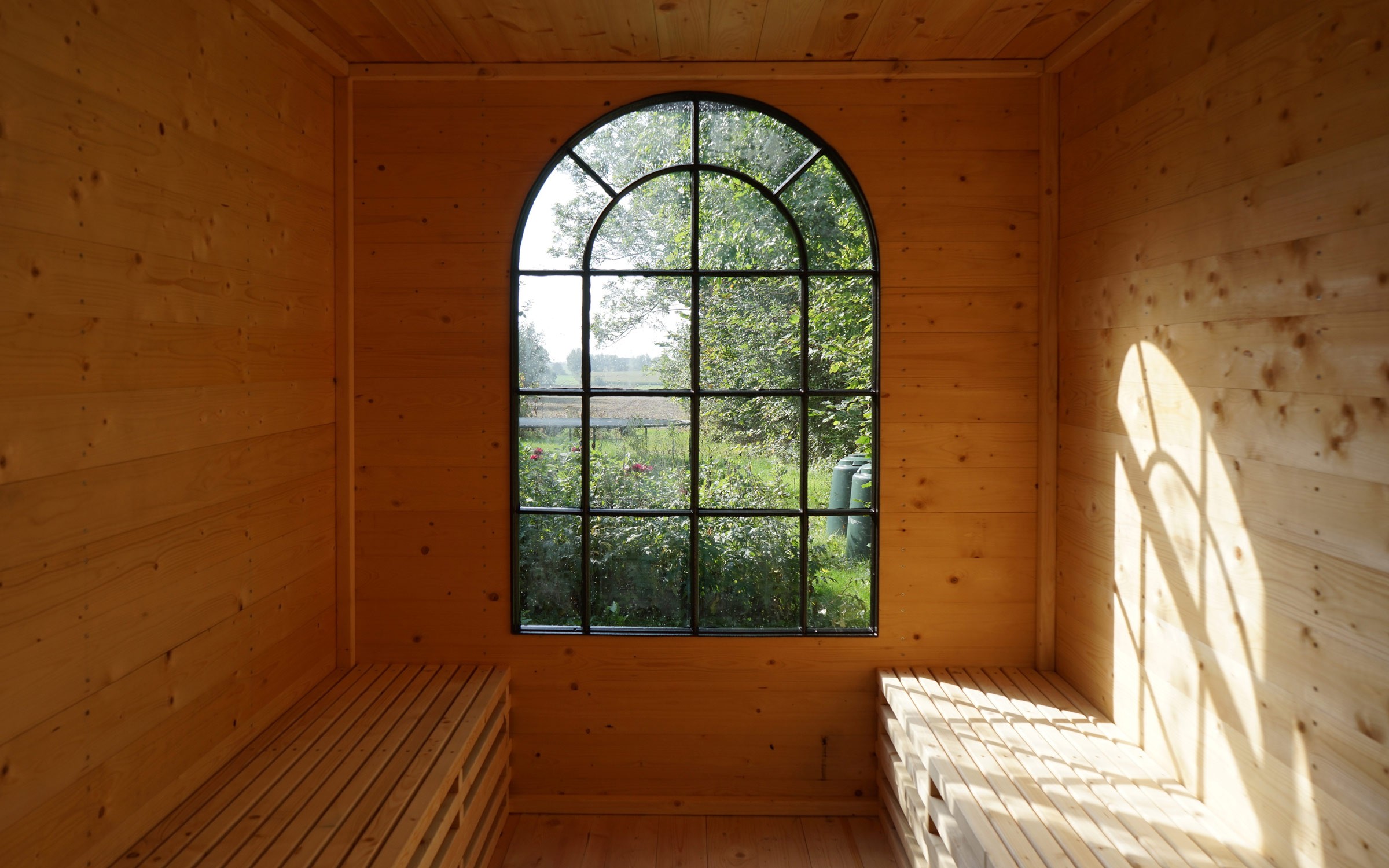 Interior of Bakkely Sauna and Guest House with timber benches and arched window overlooking garden designed by Asger Risborg 