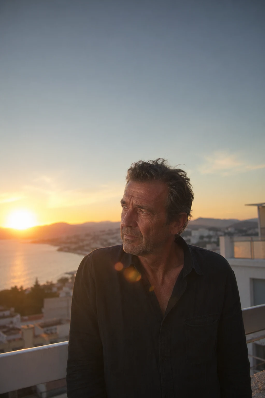 Man standing on a balcony overlooking the coast during a warm sunset with city and ocean views in the background
