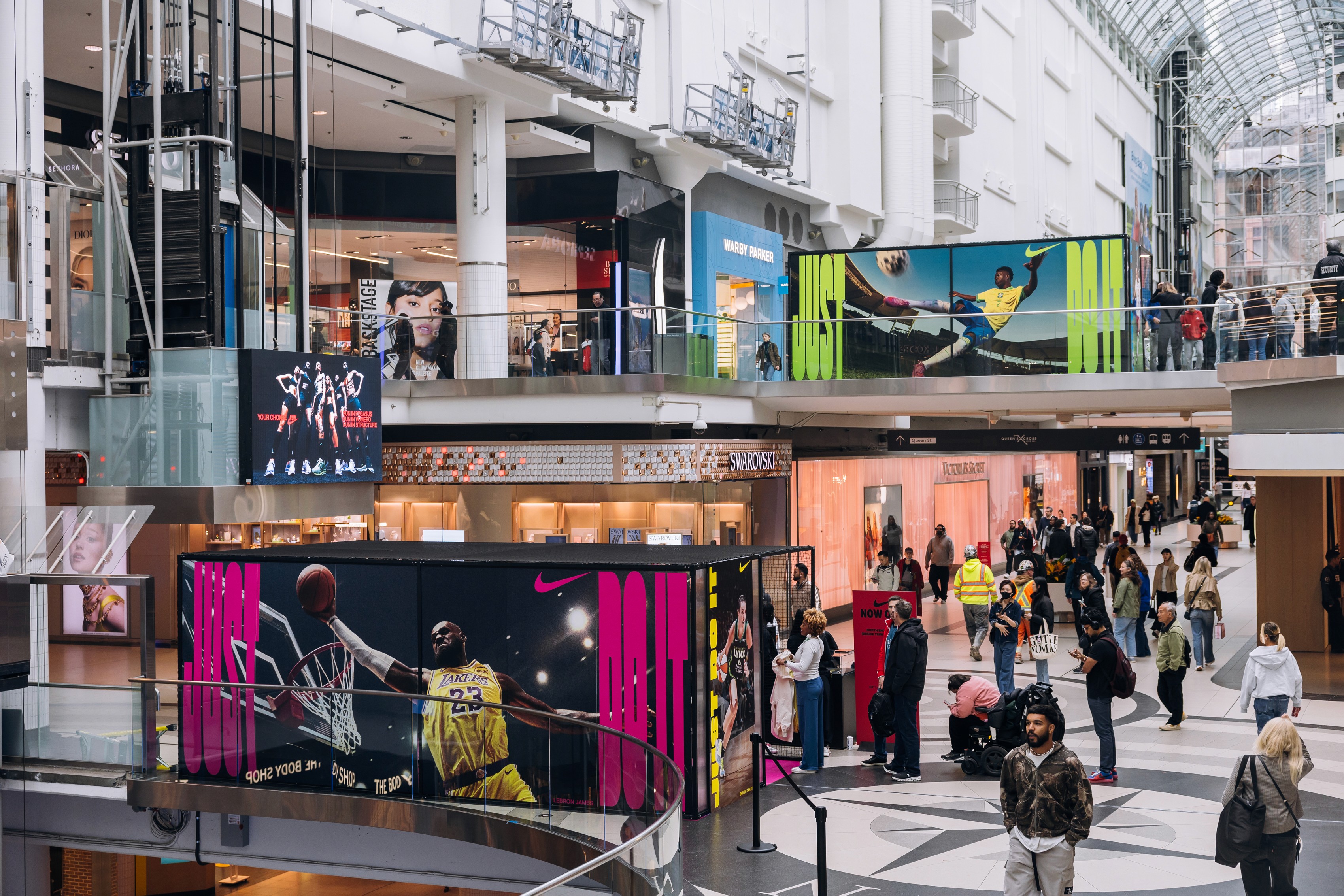 A lively scene at Eaton Centre, showcasing people shopping and walking, with Nike prominently displayed in the background.