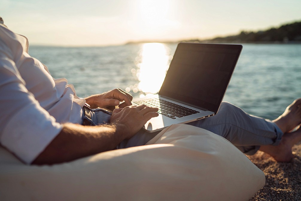 man working on a laptop on vacation relaxing oceanside beach