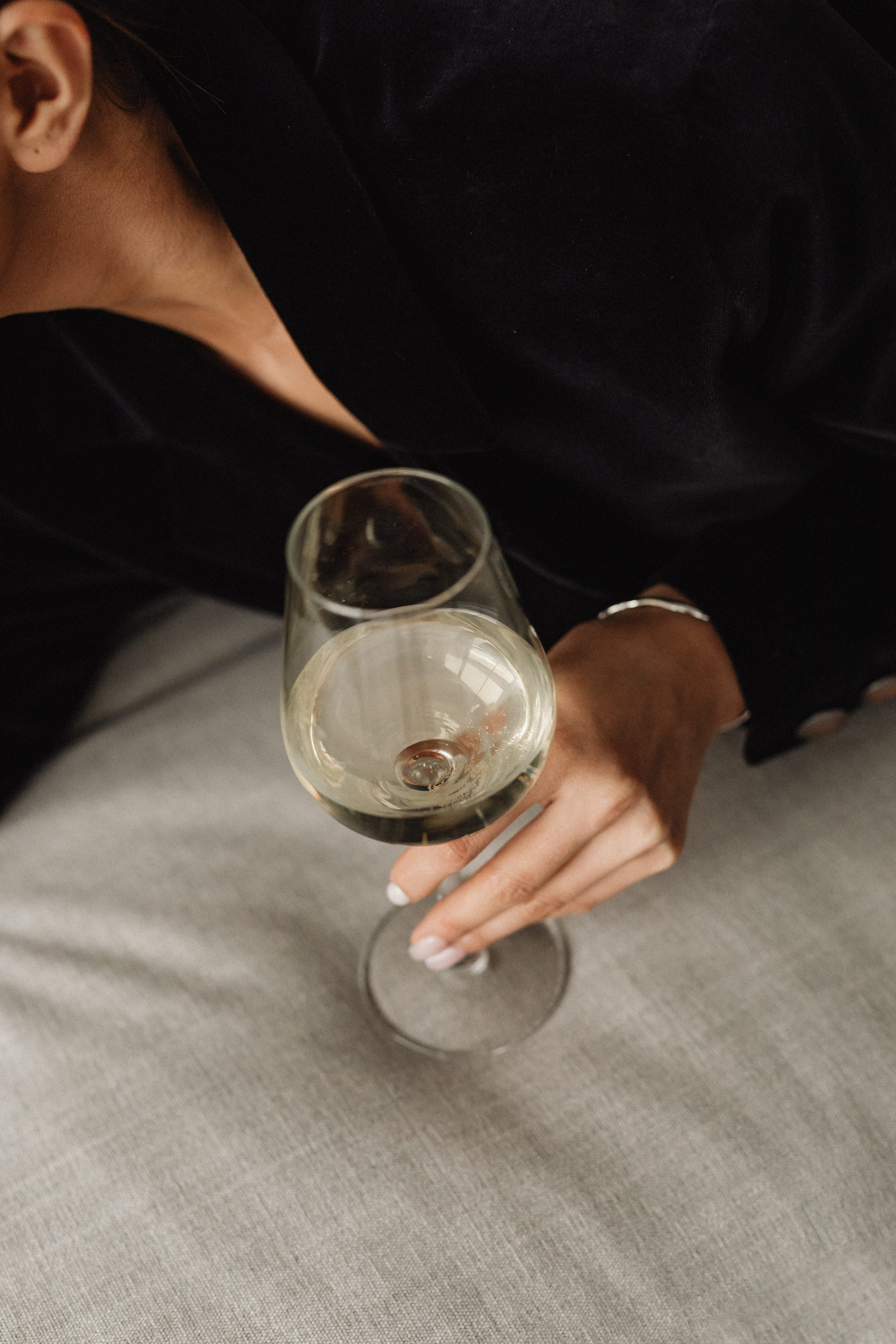 Frau in Schwarz gekleidet auf heller Oberfläche liegend mit Weinglas in der Hand 