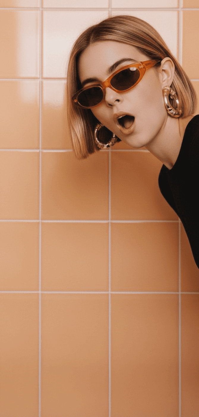 A person in a suit stands on a vintage computer, holding a phone, with a minimalist background and colorful sneakers.