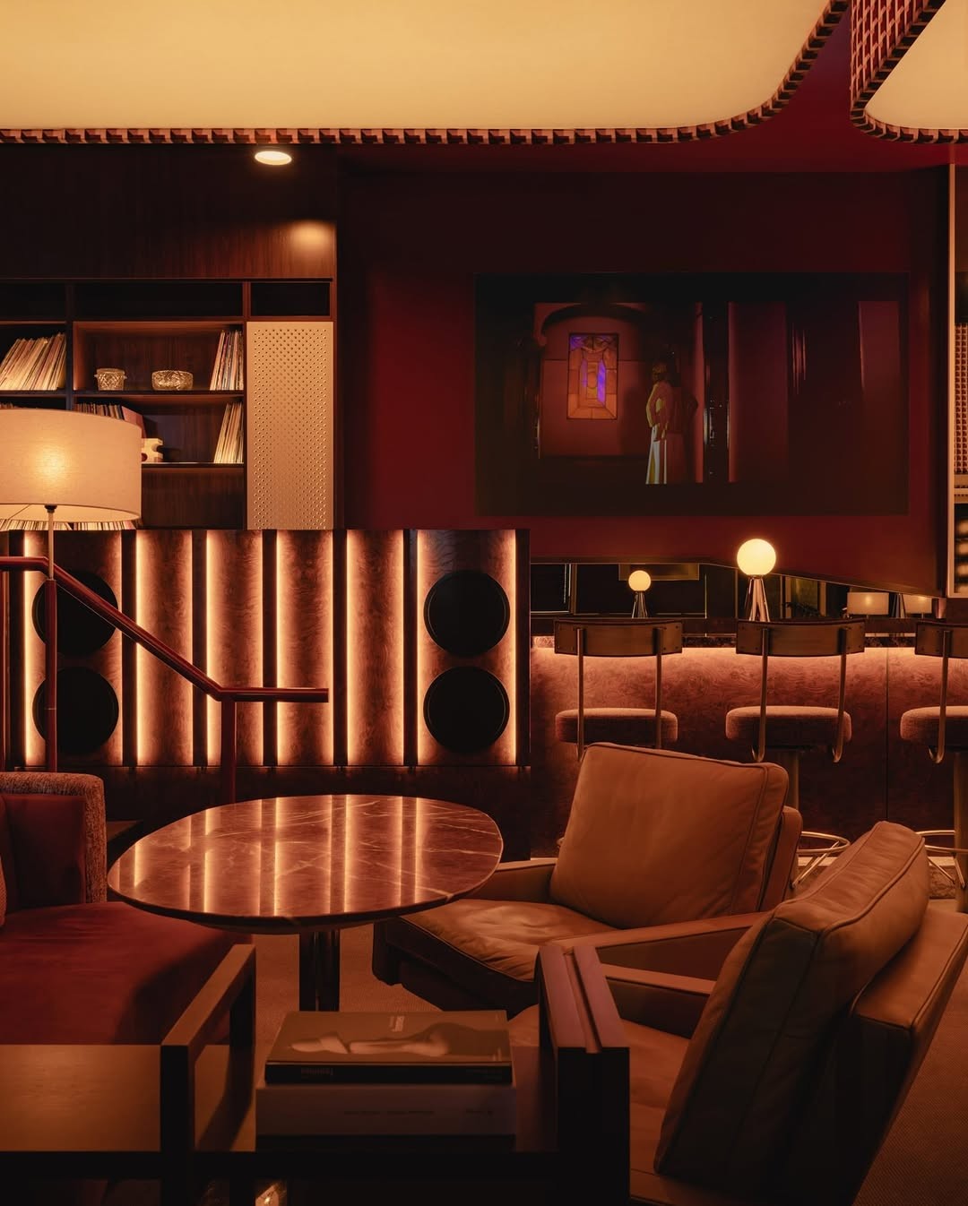 Red-toned lounge with speakers, record shelves, a projection screen, and low leather seating.