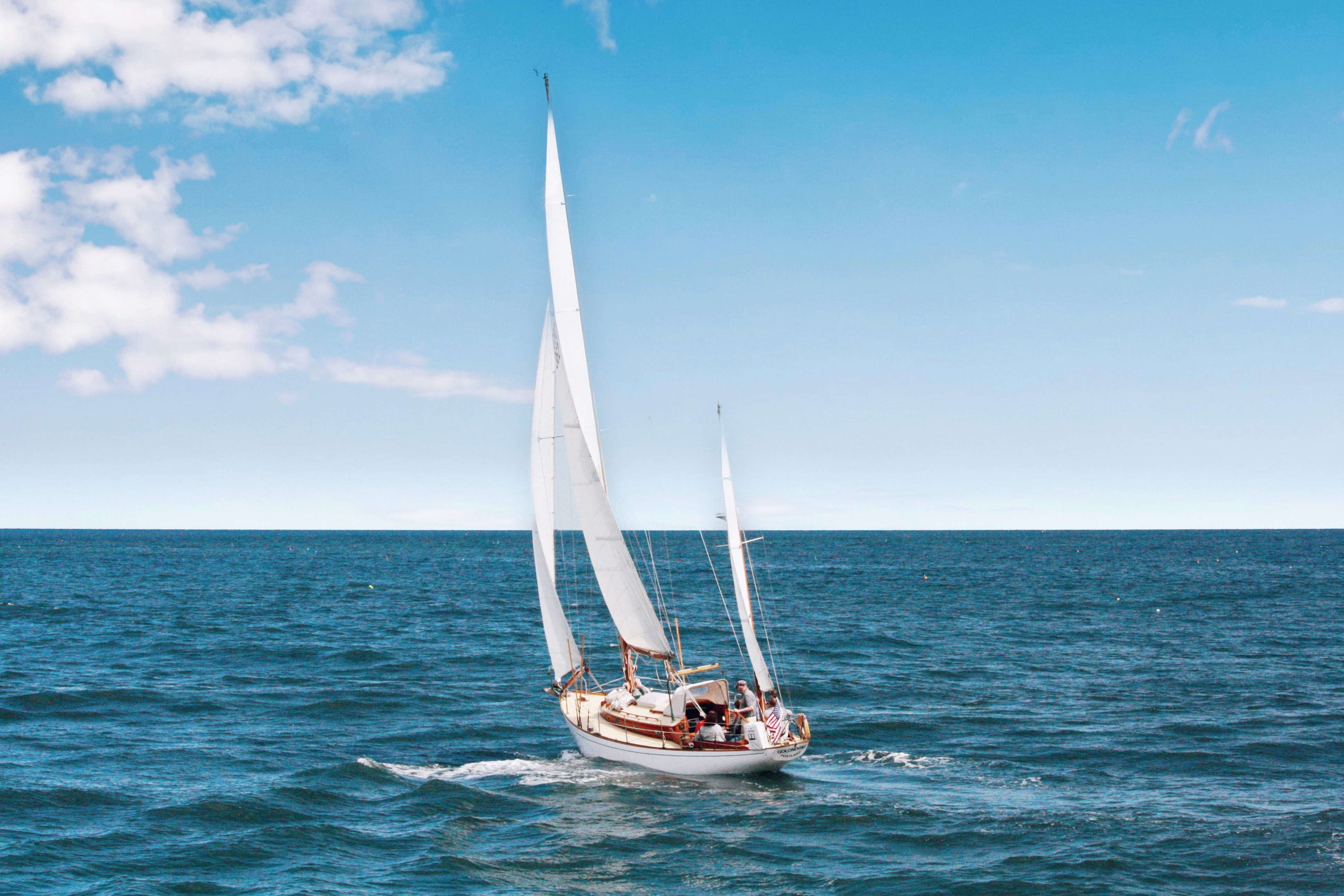 A classic two-masted sailboat heeling in a steady breeze under a blue sky