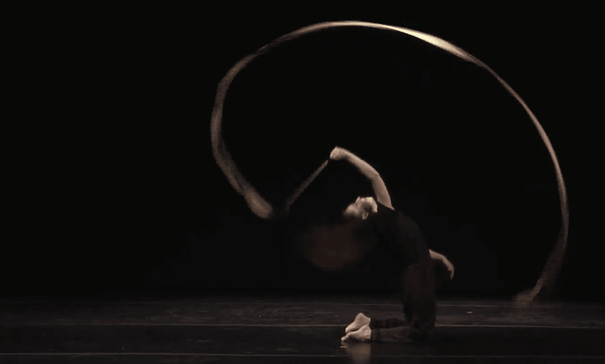 A dancer on a dark stage under a golden arc of light