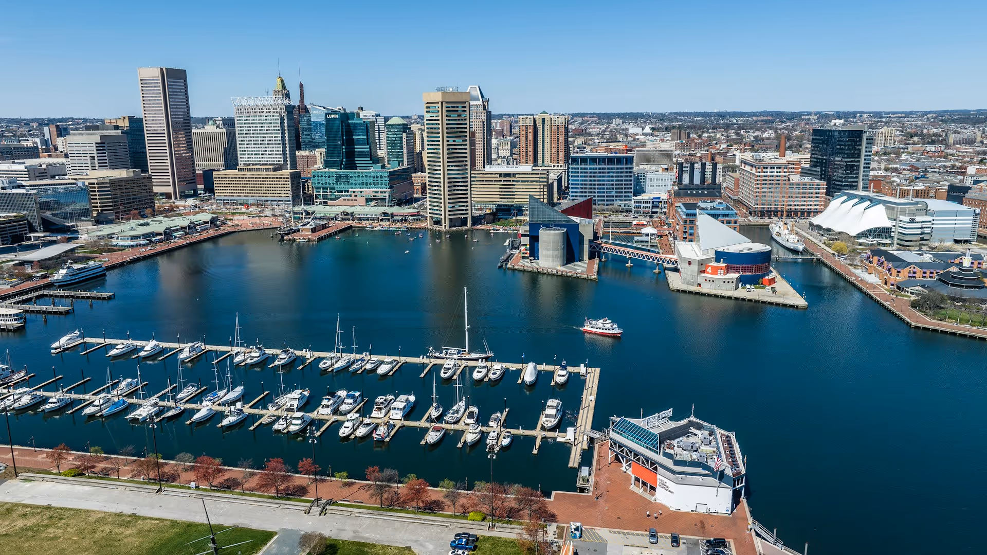 Aerial view of Baltimore Inner Harbor with marina, skyline, and waterfront buildings.