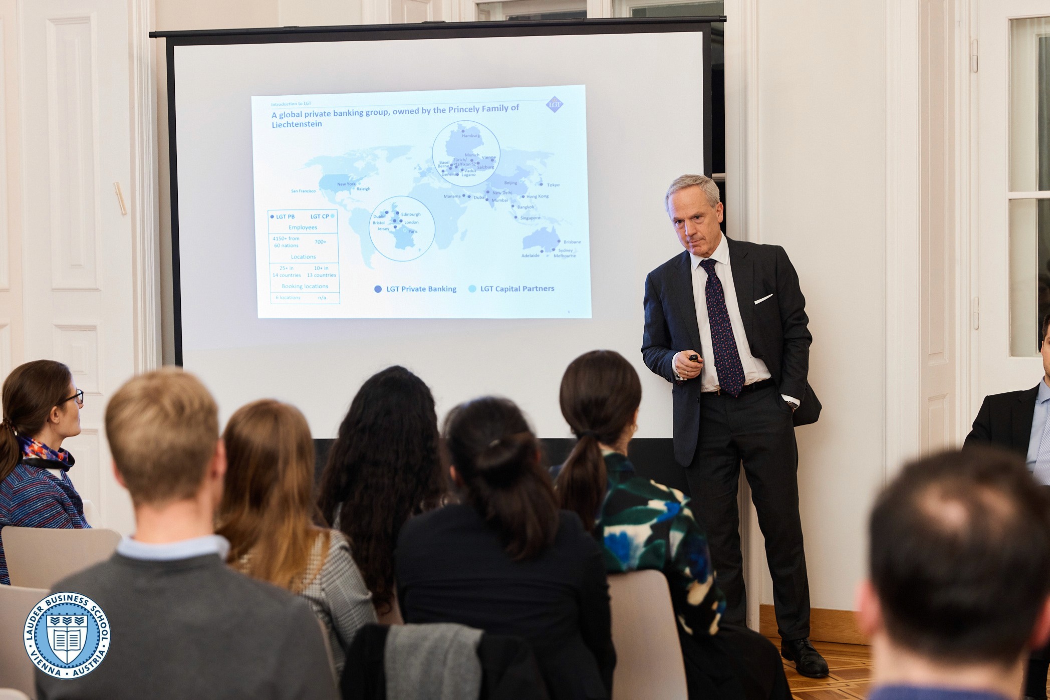 Group of LBS students sitting together, smiling and discussing while using a laptop in a modern campus setting