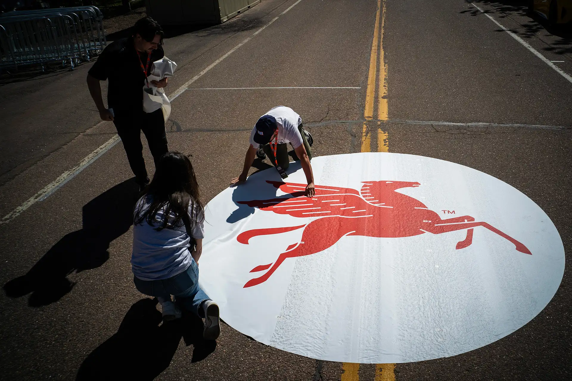 Three people applying a large Mobil 1 Pegasus decal to pavement.