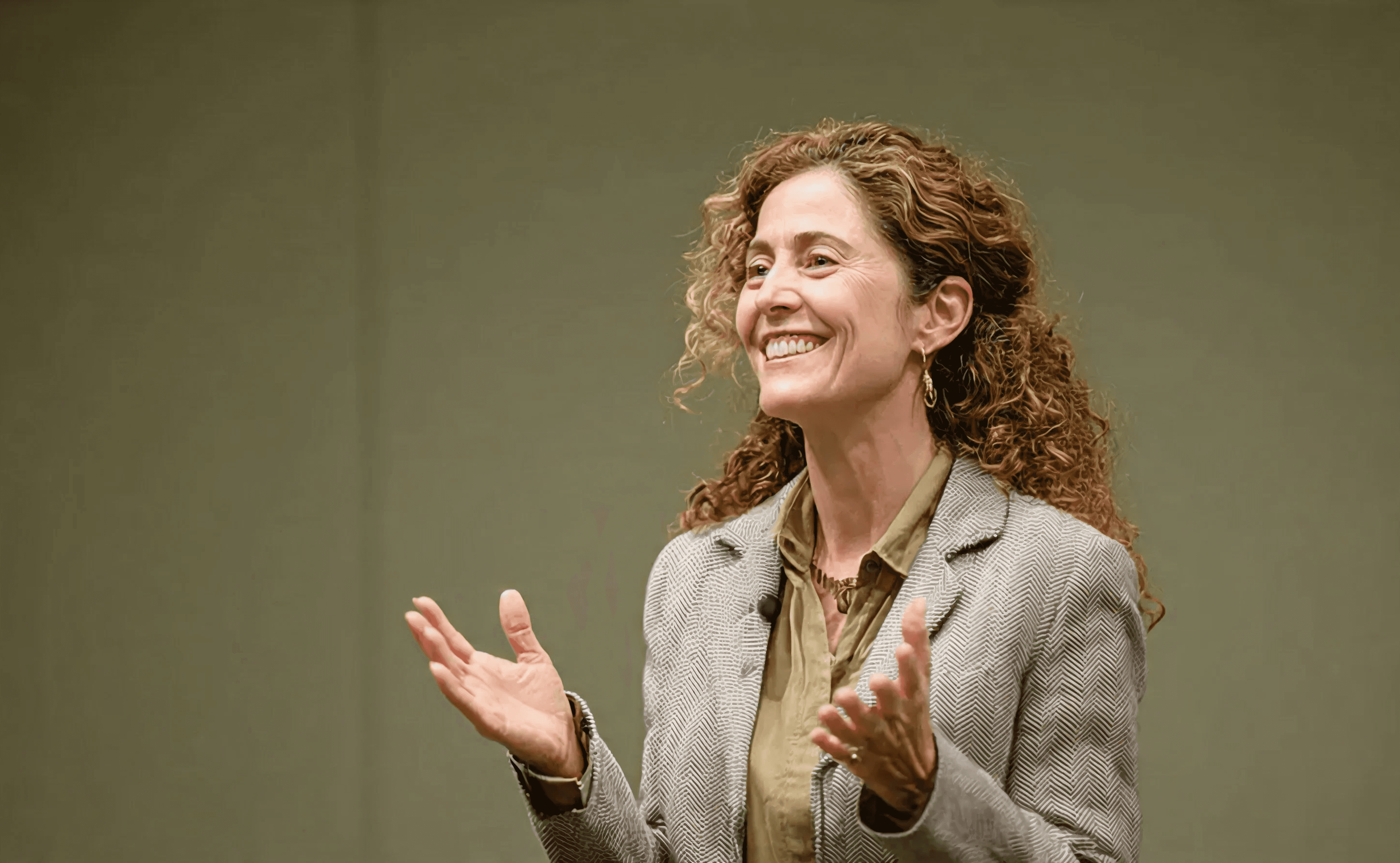 Cheerful, mature woman speaker with curly hair gesticulates warmly at an event.