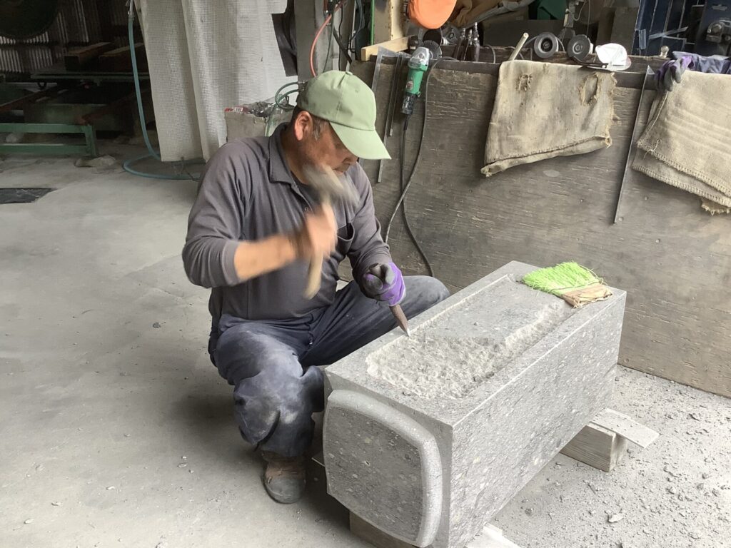 A craftsman manually chiseling a stone block in a workshop, focusing on detailed stone carving techniques.